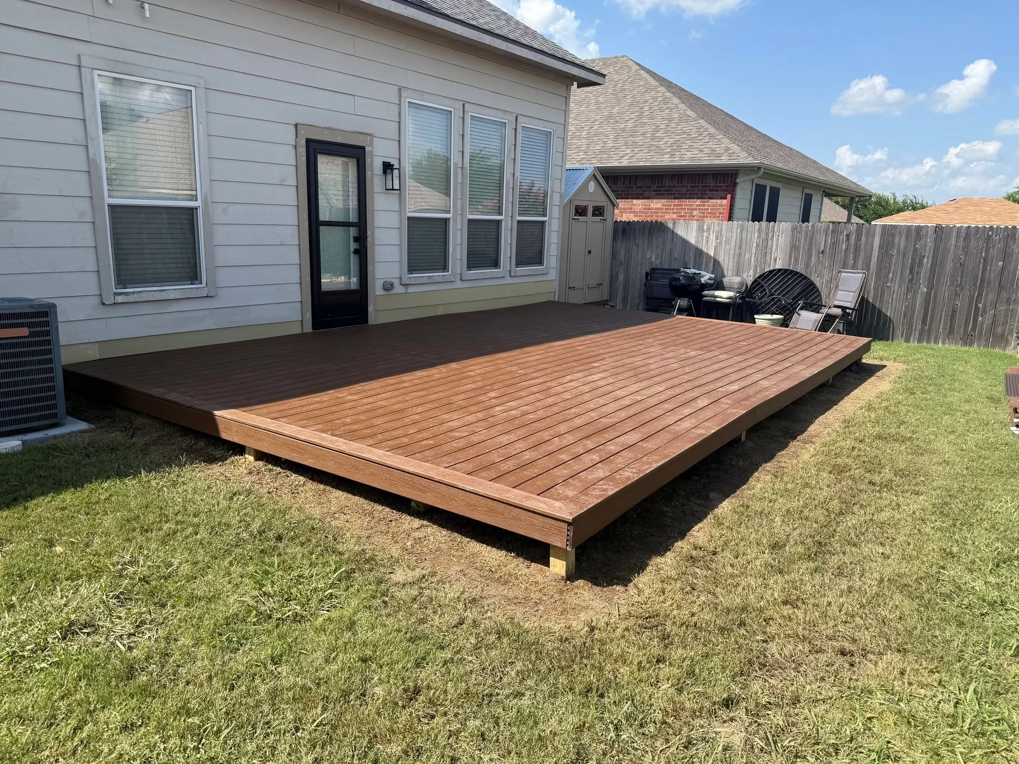 Large composite deck with linear board pattern installed at ground level against residential home