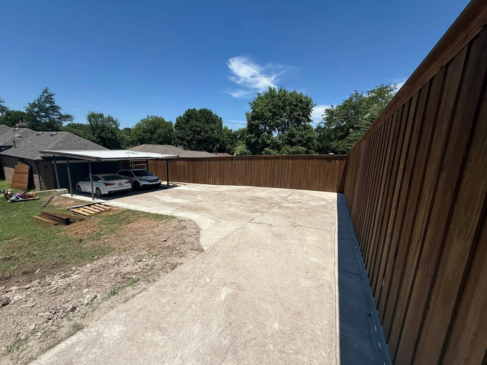 Corrugated metal privacy fence with concrete patio and carport in residential backyard