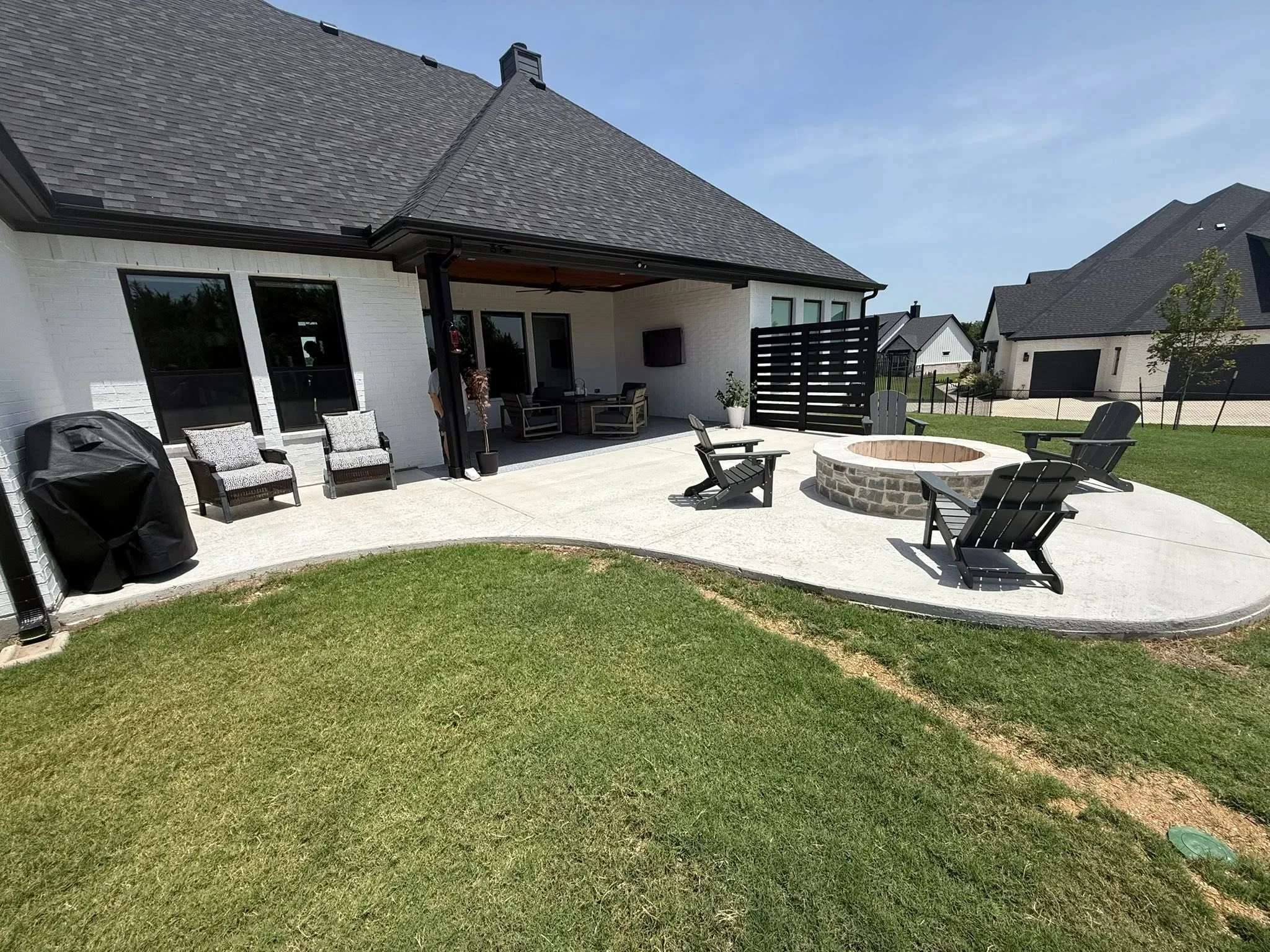 Concrete patio with fire pit, Adirondack chairs, and covered structure with black privacy screen