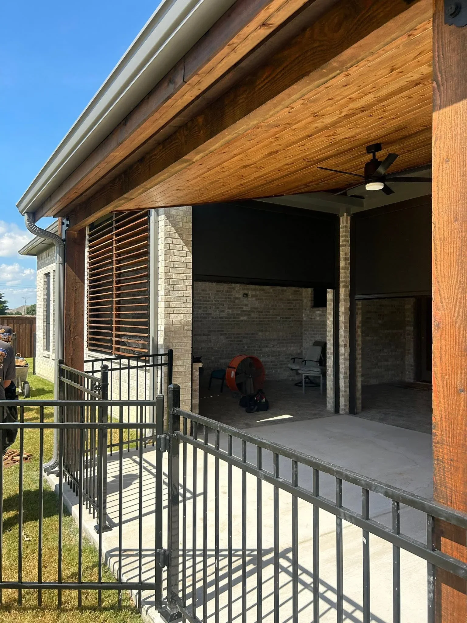 Stained wood pergola with horizontal slats and black metal railing on concrete patio
