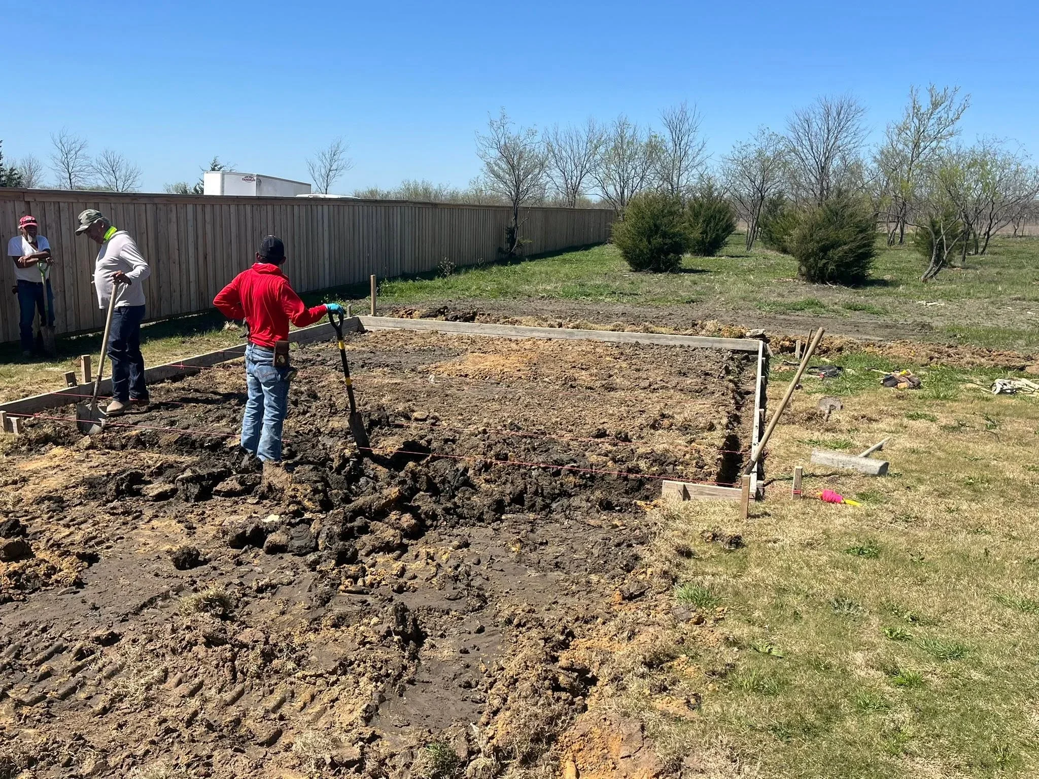 Excavated soil and prepared ground with wooden markers for fence foundation layout