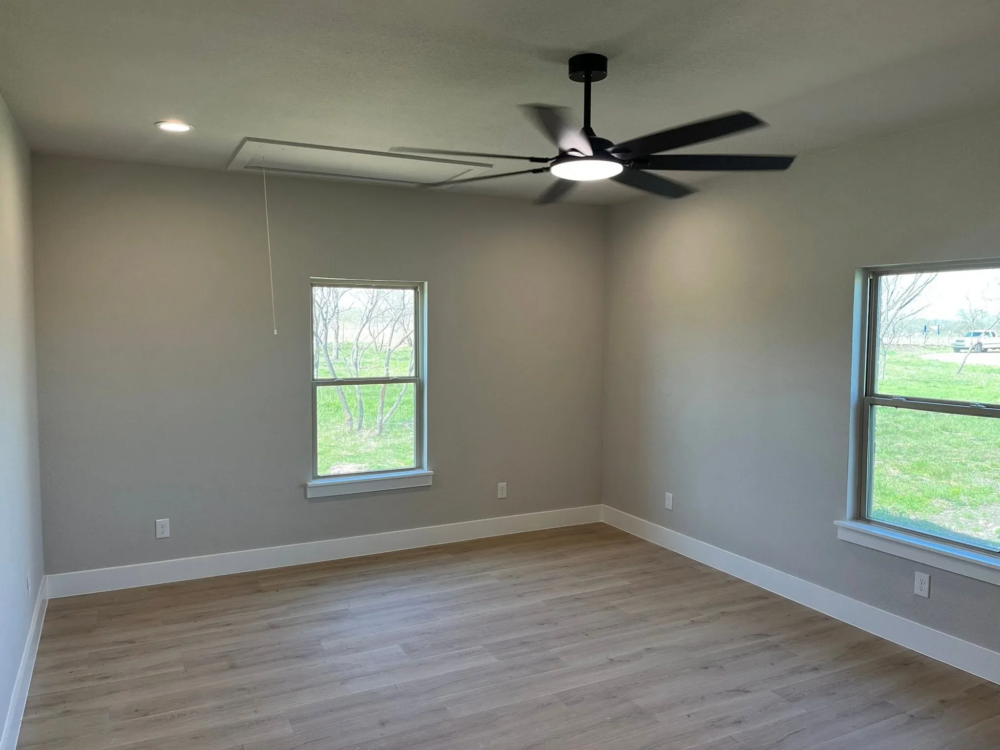 Finished interior room with drywall, white trim, hardwood flooring, and ceiling fan installation