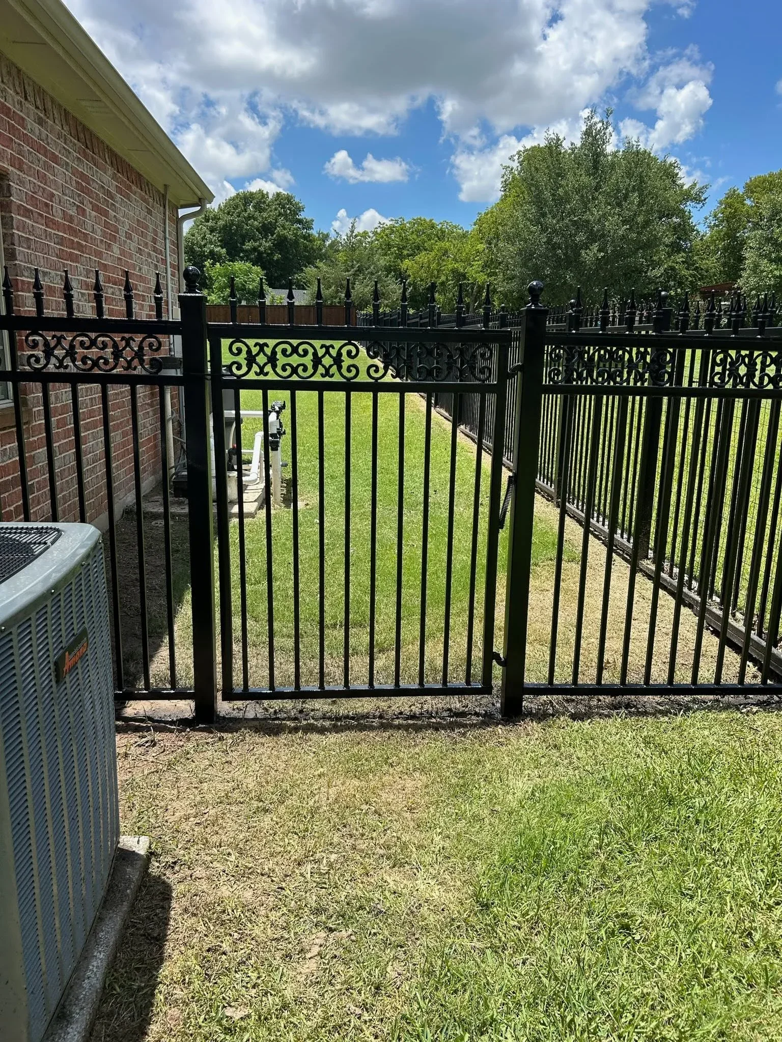 Black ornamental iron fence with scrollwork design and matching gate installed along brick home