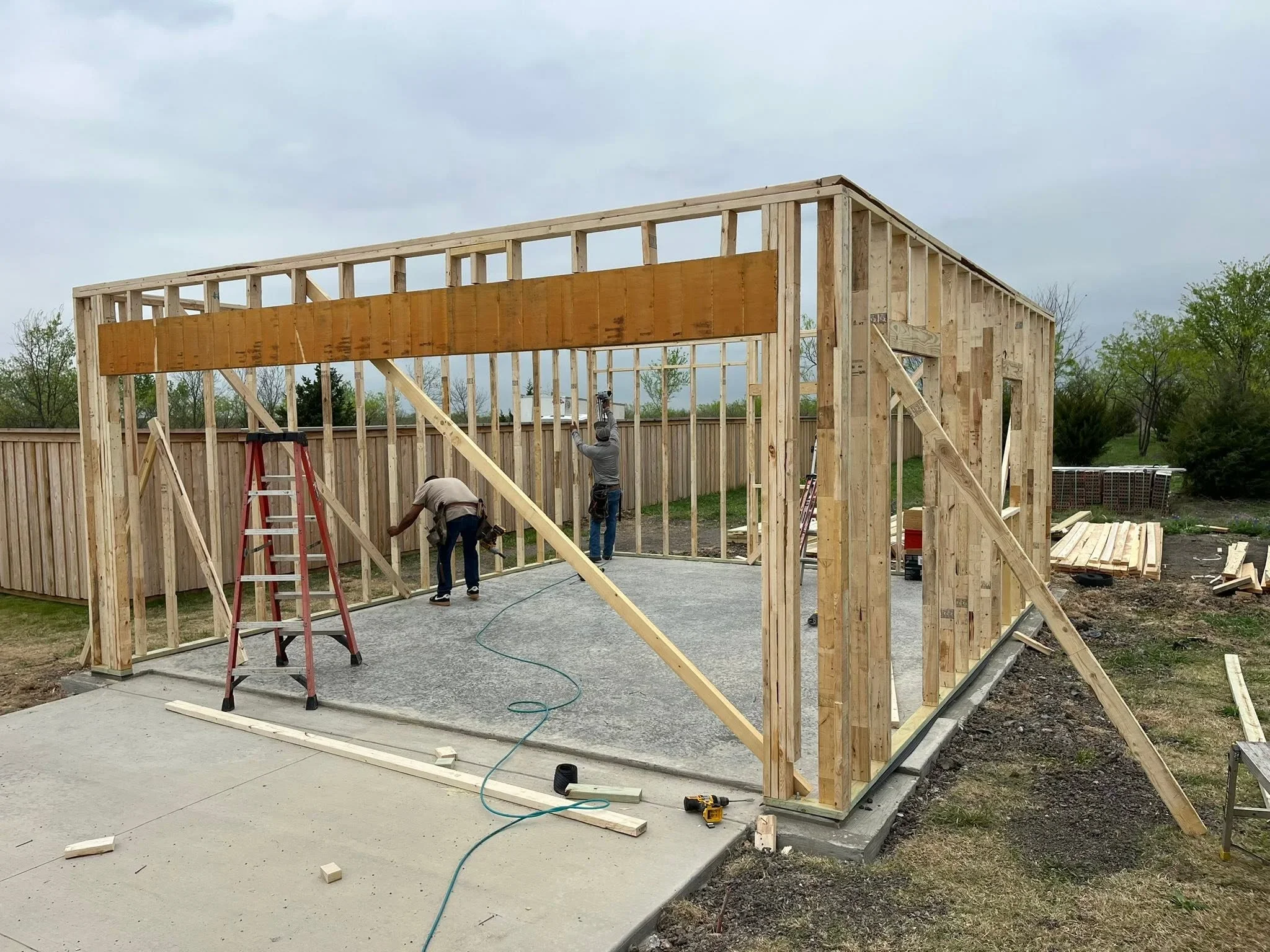 Wood-framed residential building under construction with lumber framing, concrete slab, and diagonal bracing