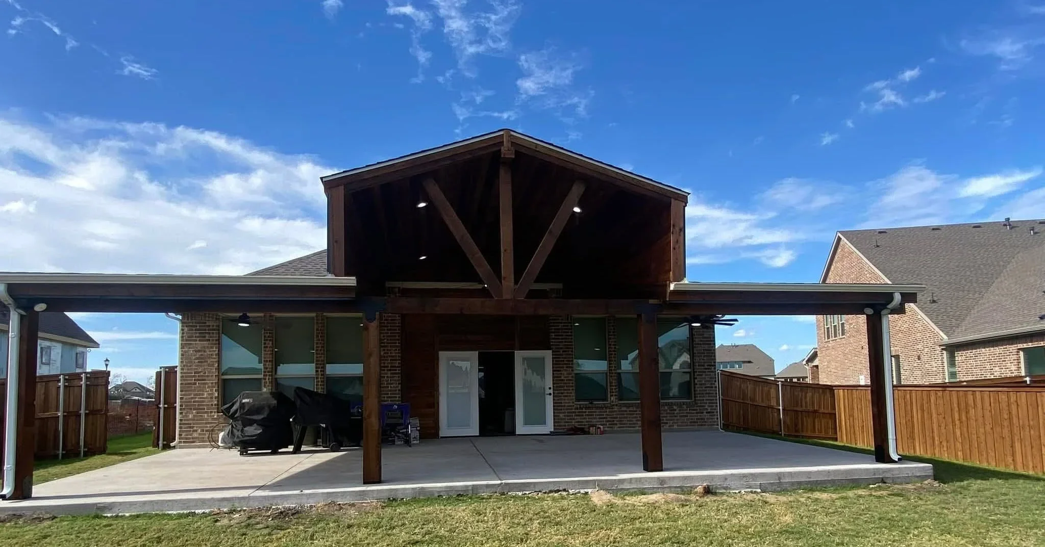 Covered patio with gable roof, timber beams, composite decking, and brick columns