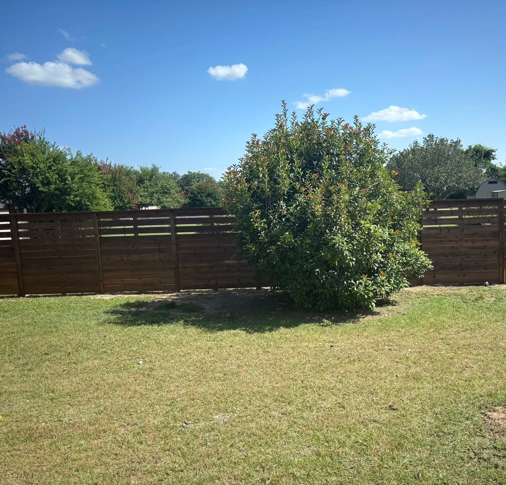 Dark horizontal wood fence with horizontal slats installed in residential backyard with mature trees