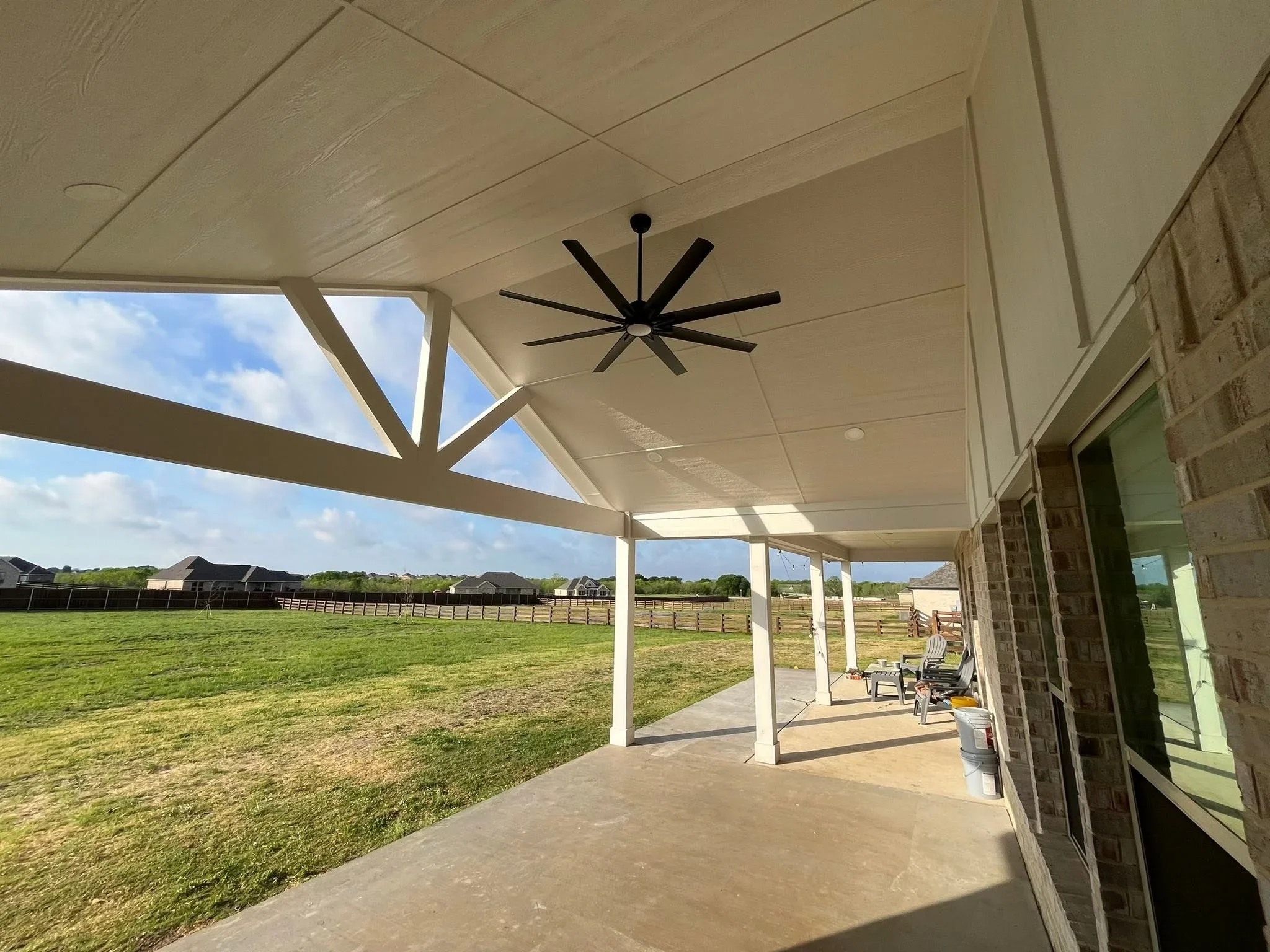 White aluminum patio cover with coffered ceiling, black ceiling fan, concrete pad, and rural property views