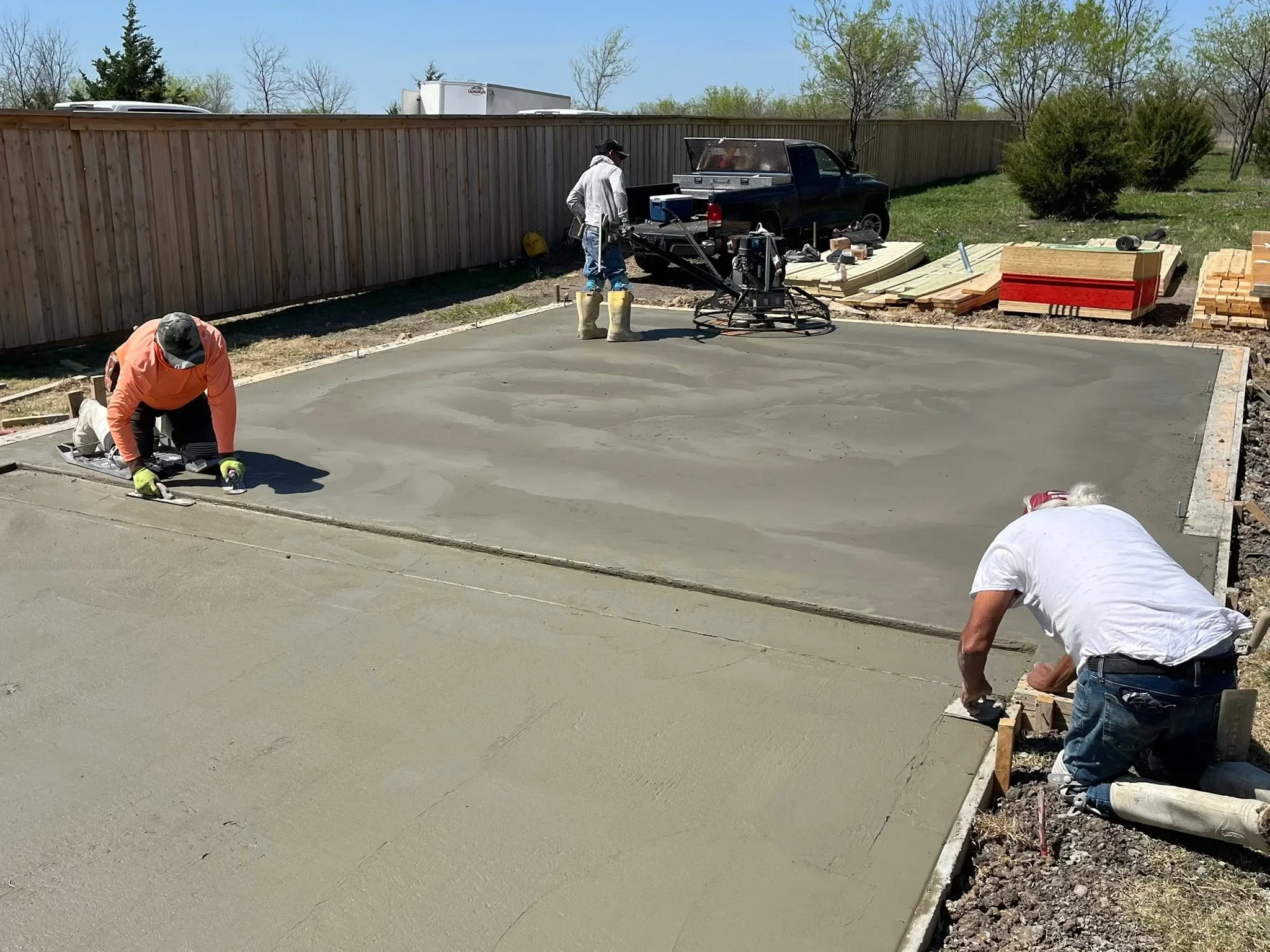 Concrete pad installation with workers finishing fresh concrete and wooden frame forms