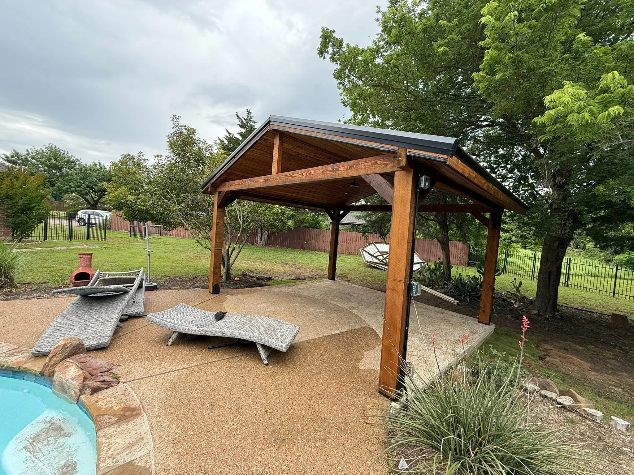 Wooden pergola with metal roof over composite patio and cornhole setup in backyard