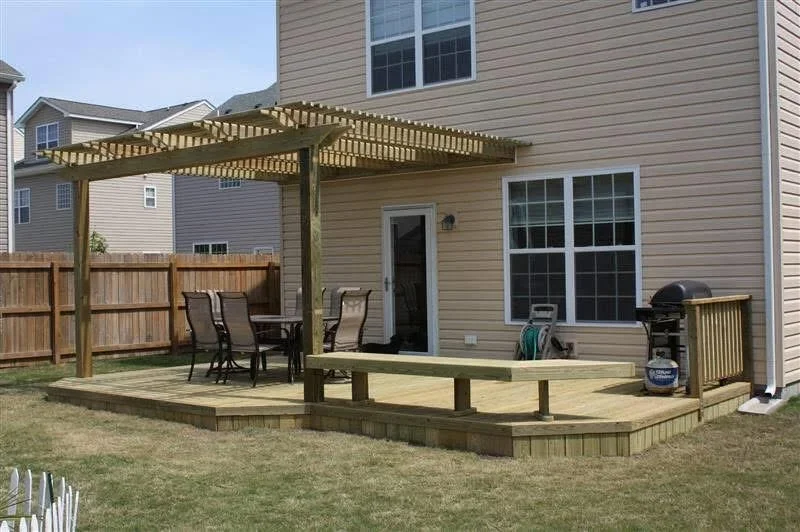 Composite deck with pergola, bench seating, and wooden privacy fence attached to house