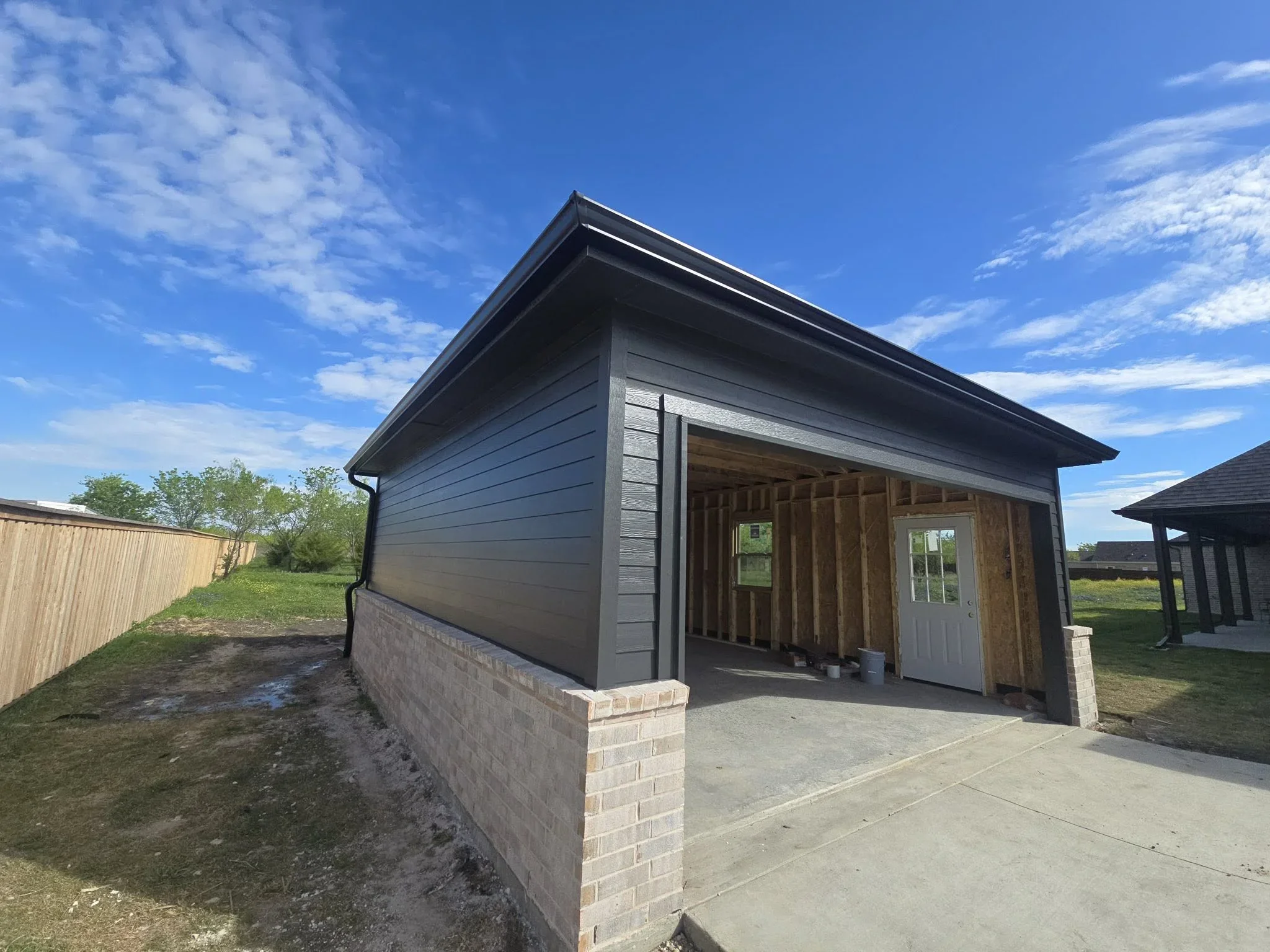 New garage with gray horizontal siding, brick foundation, and concrete driveway