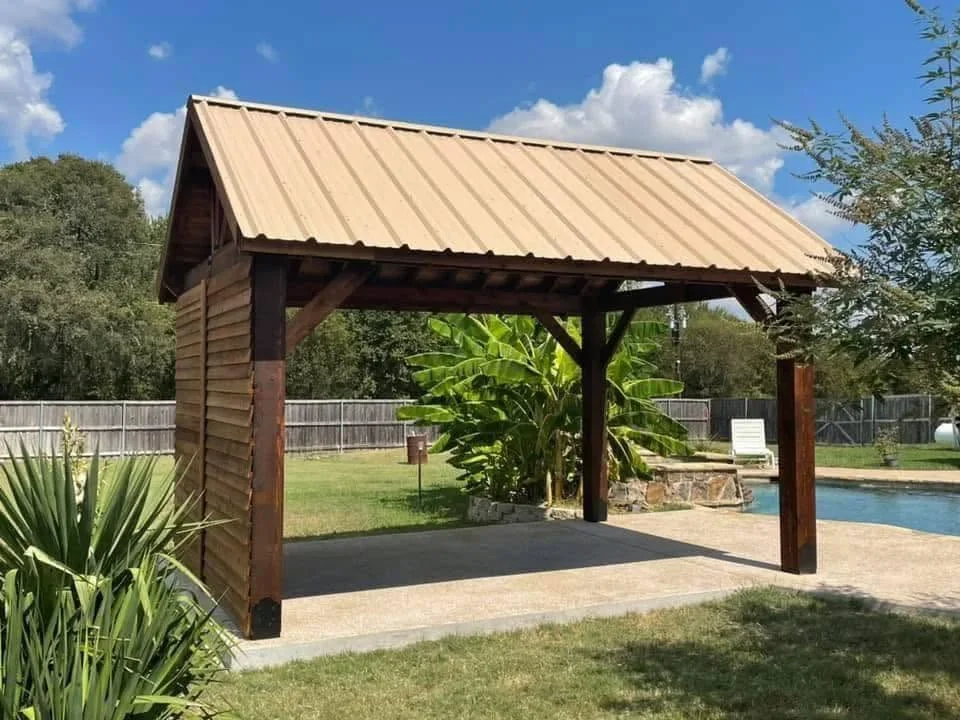 Covered patio with tan metal roof, wood posts, and concrete pad near pool