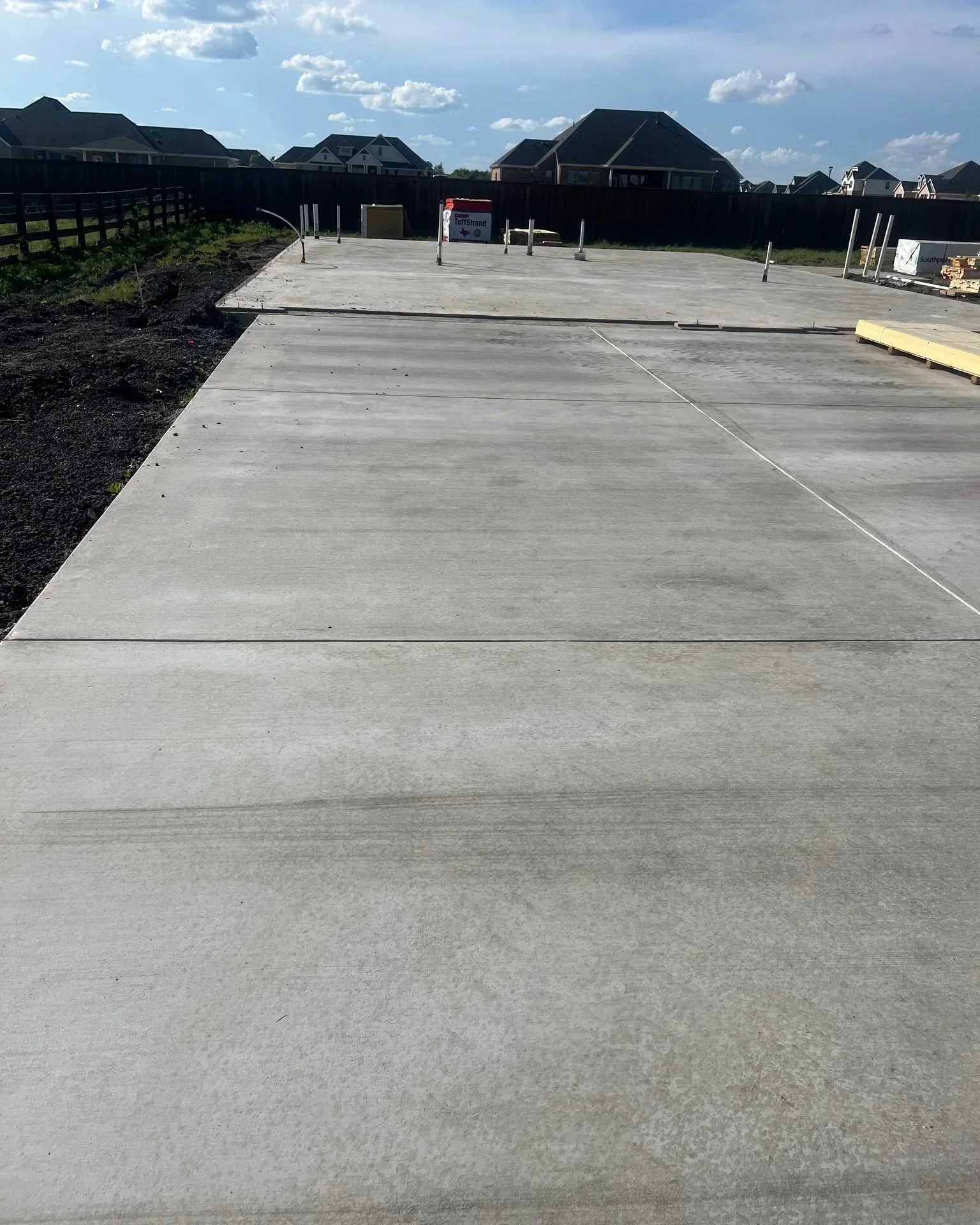 Newly poured concrete driveway with control joints and wooden post markers in residential area