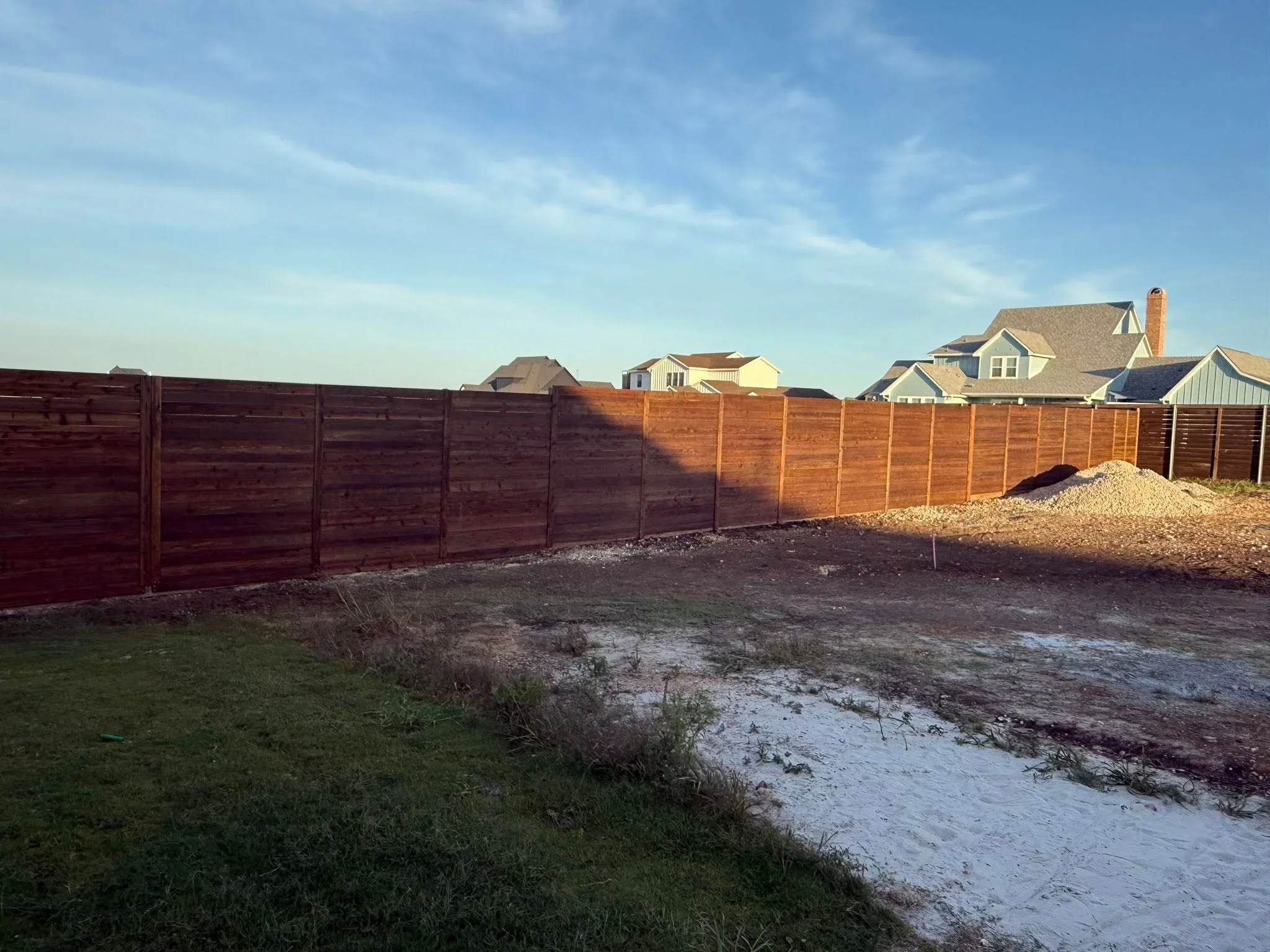 Newly installed wood privacy fence with stained cedar panels and gravel base