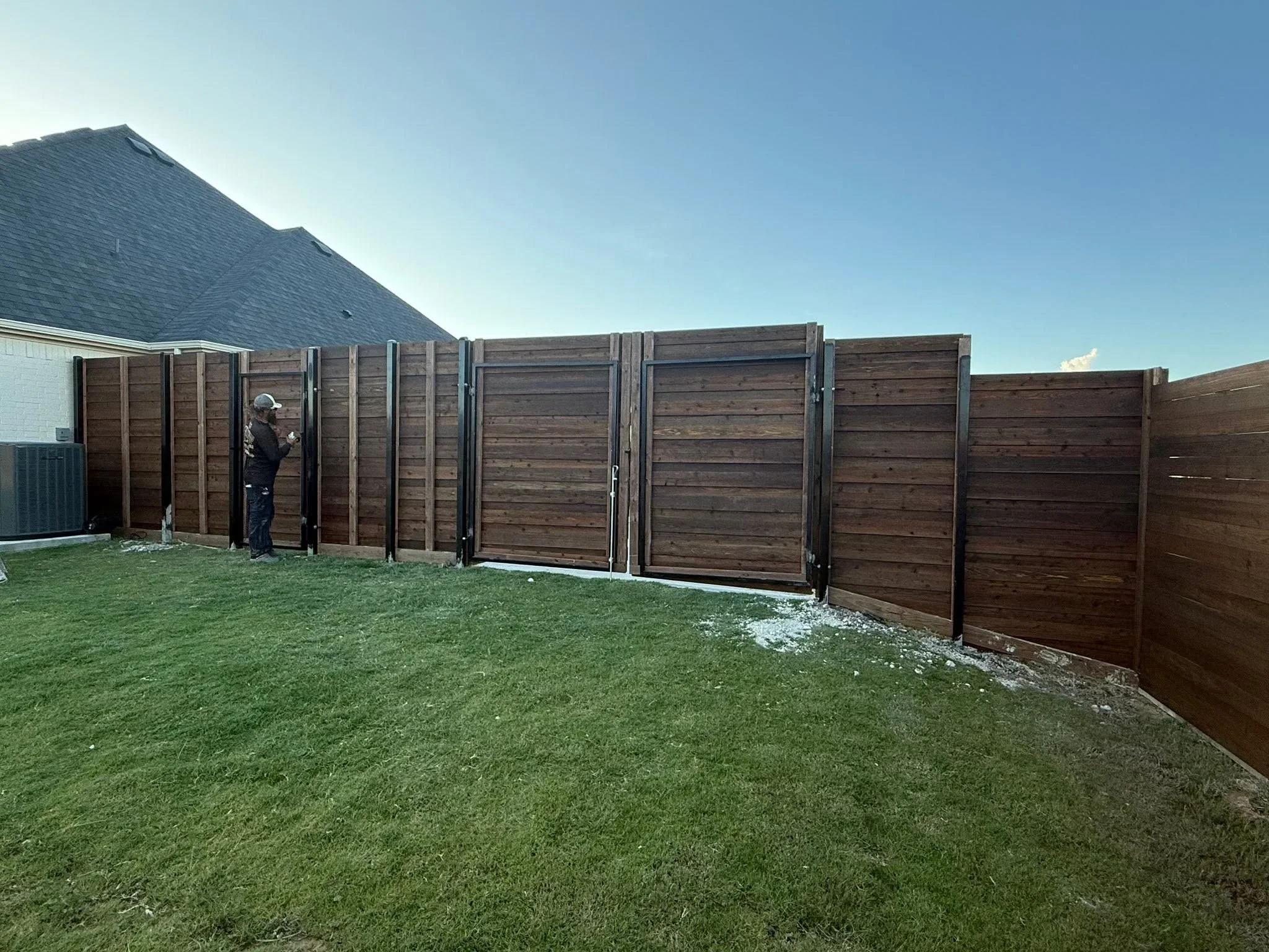 Horizontal stained wood privacy fence with metal posts and gates installed along residential backyard