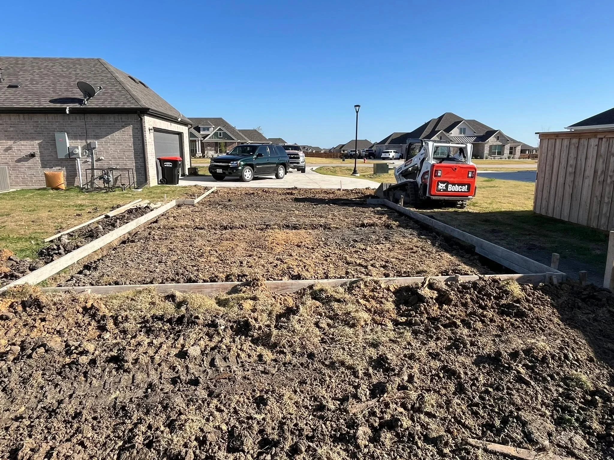Excavated residential driveway with wooden frame borders and Bobcat equipment on-site