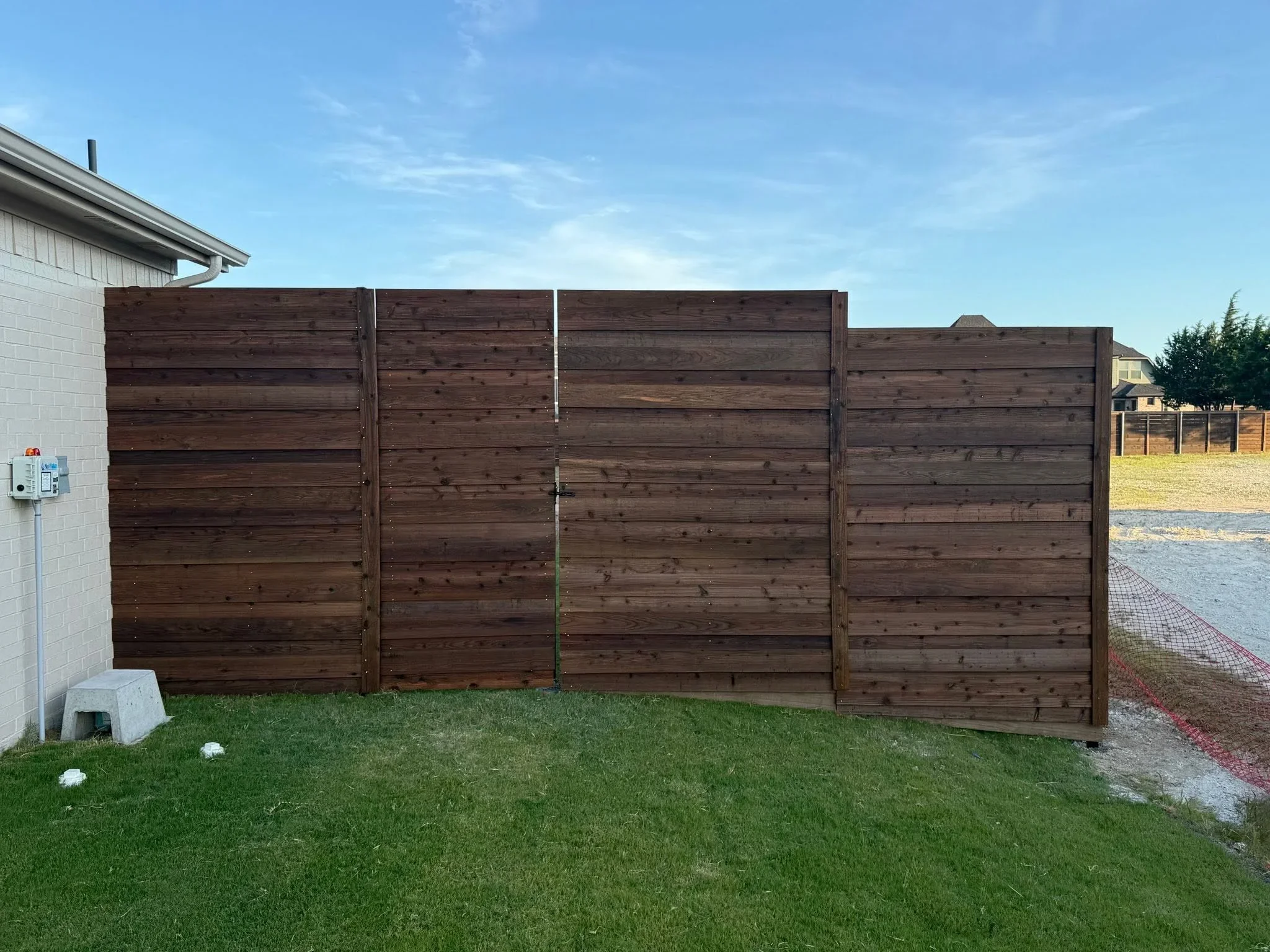 Dark stained horizontal wood privacy fence with cedar boards and post construction in residential backyard