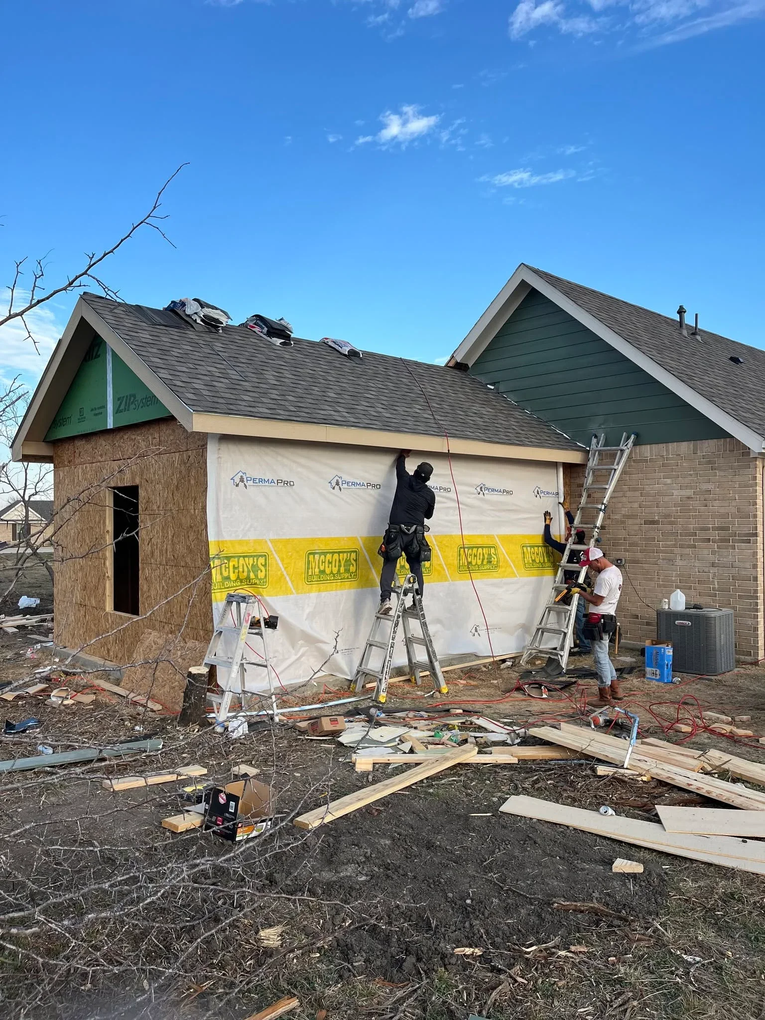 Roof replacement in progress with new shingles, protective sheeting, and worker on ladder