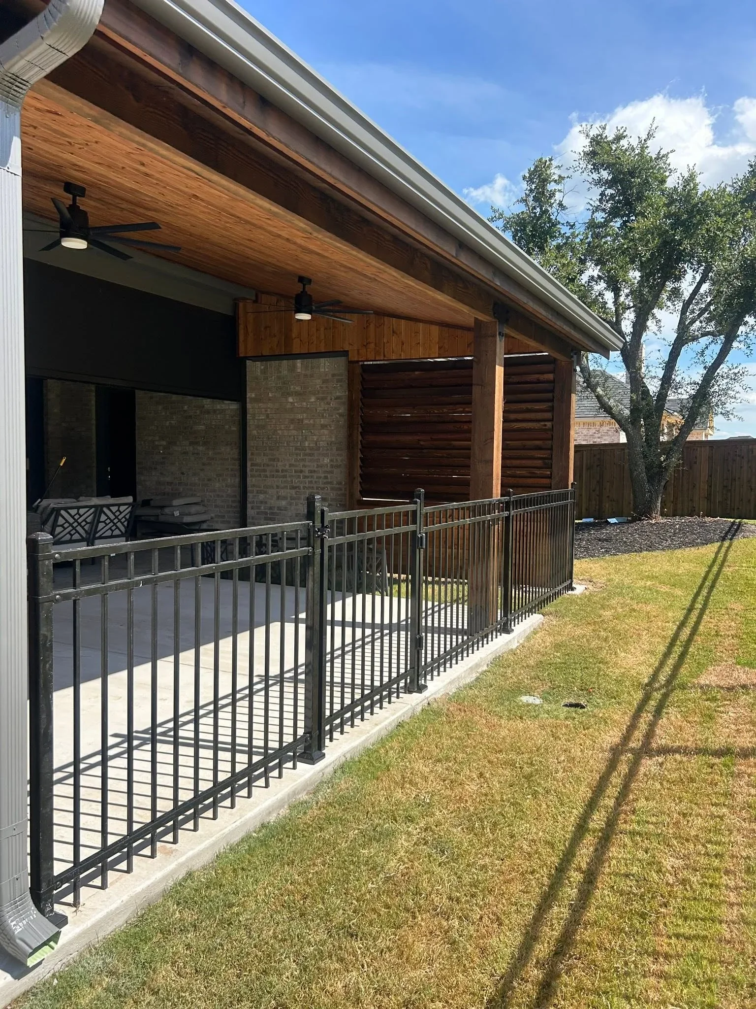 Black metal vertical picket railing with gate on concrete patio, wood soffit overhead