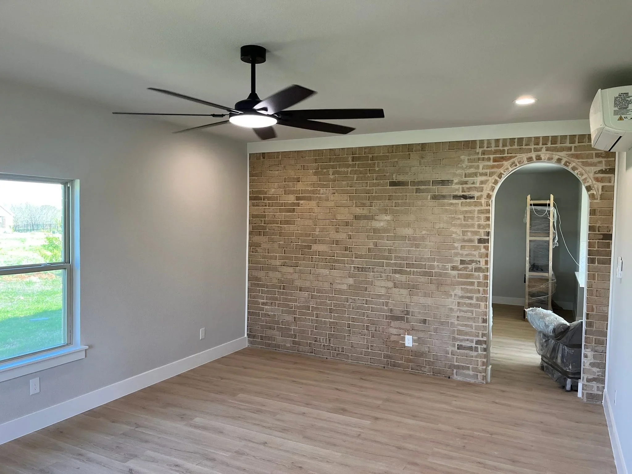 Interior room with exposed brick wall, arched doorway, drywall, hardwood flooring, and ceiling fan