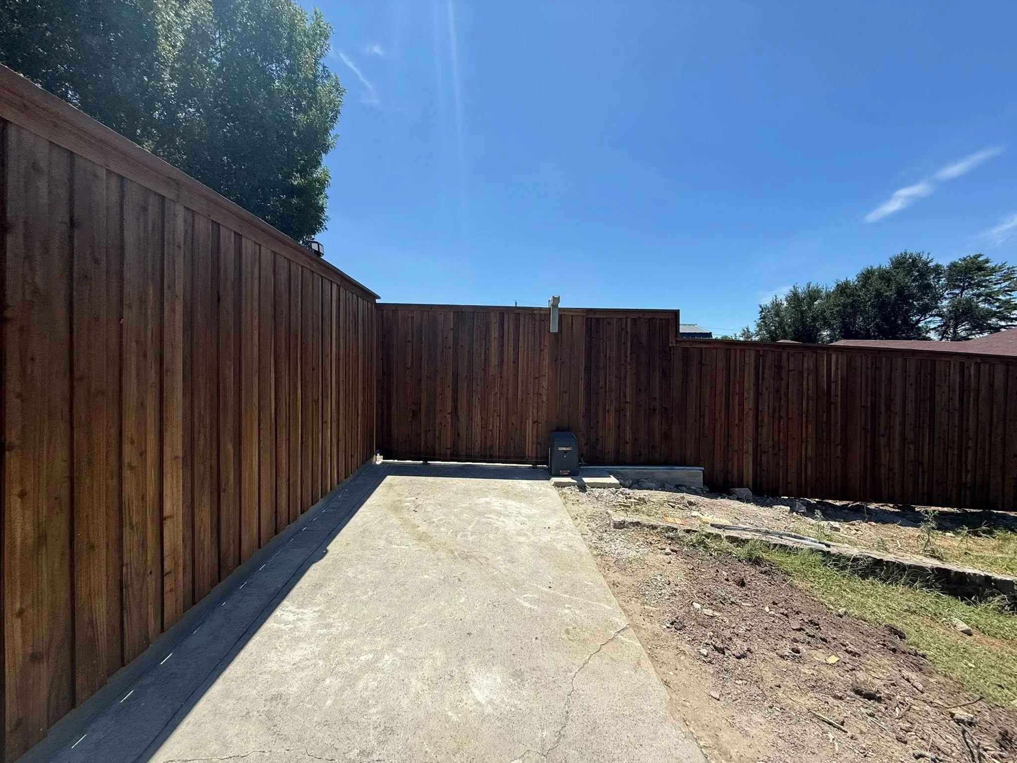 Dark stained wood privacy fence with vertical boards and concrete footer along residential property