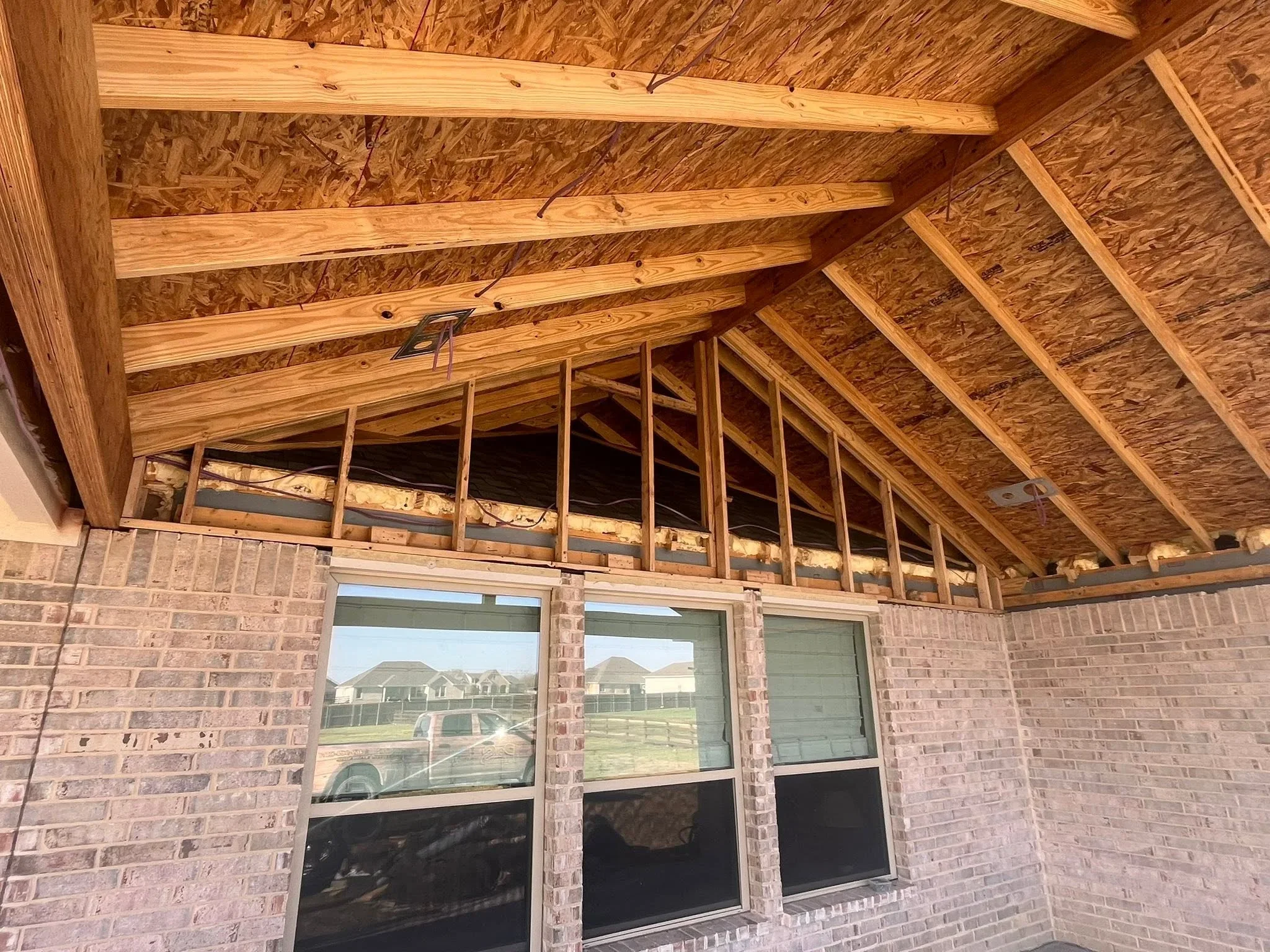 Roof framing with wooden beams and OSB sheathing over brick walls with windows