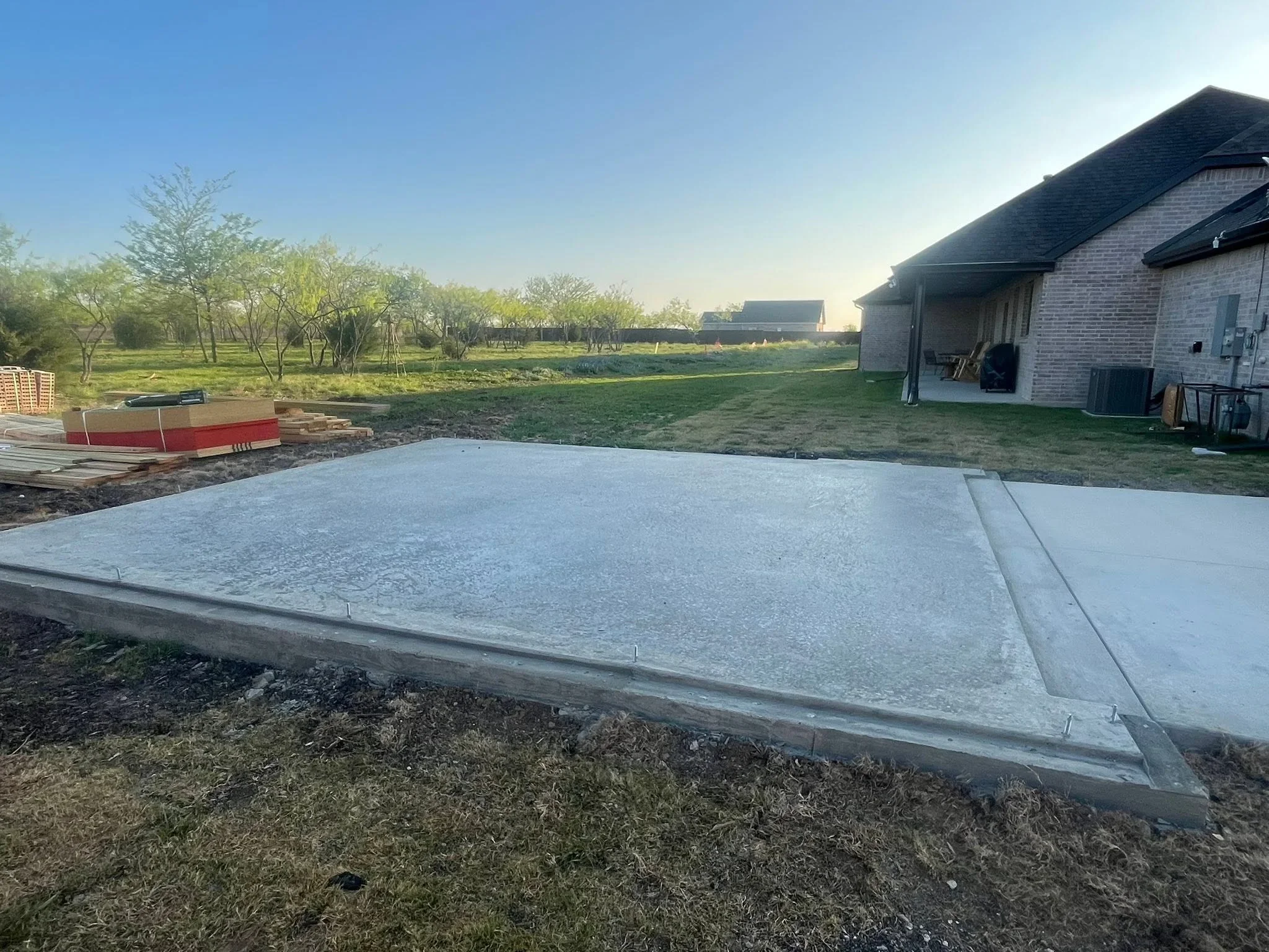Finished concrete foundation pad with control joints and concrete perimeter edge on cleared ground