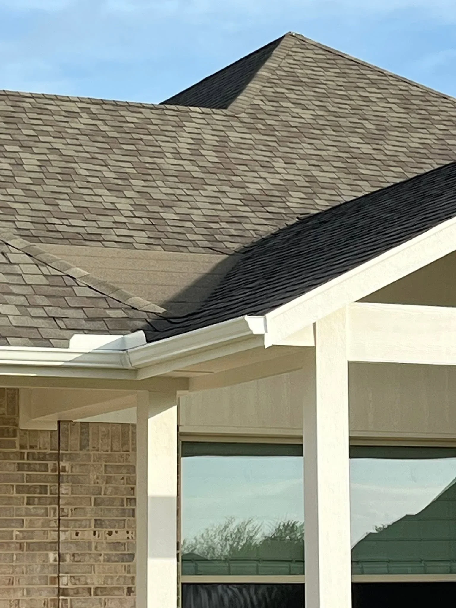 Architectural asphalt shingle roof with gray and charcoal shingles, white fascia trim, and brick exterior