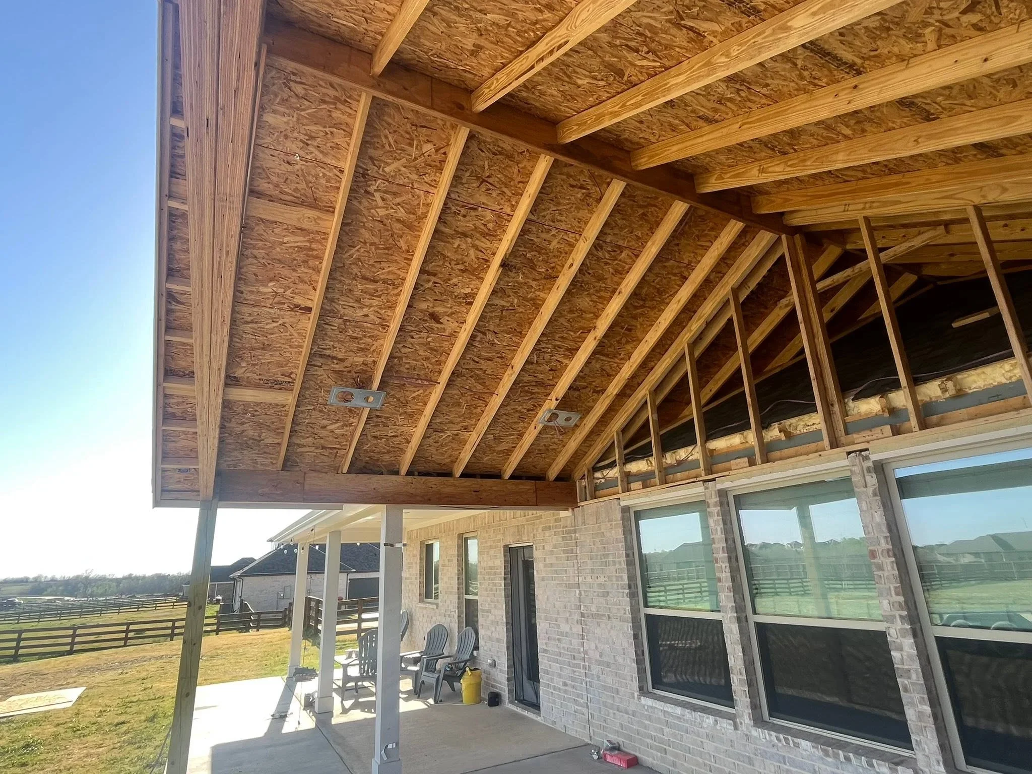 Covered patio with exposed wood beam framing, OSB sheathing, brick walls, and large windows