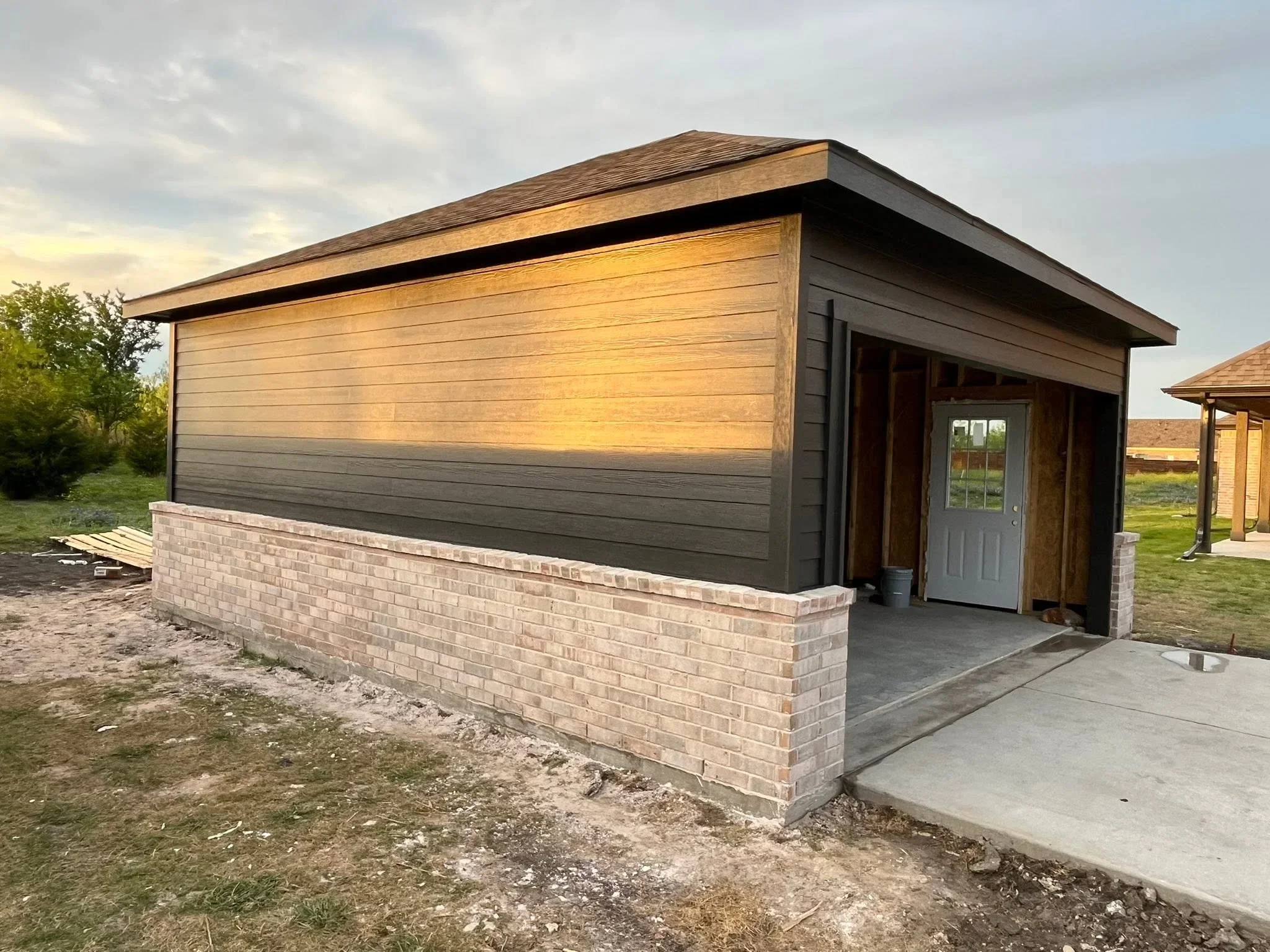Modern garage with horizontal wood siding, brick foundation, and pitched roof