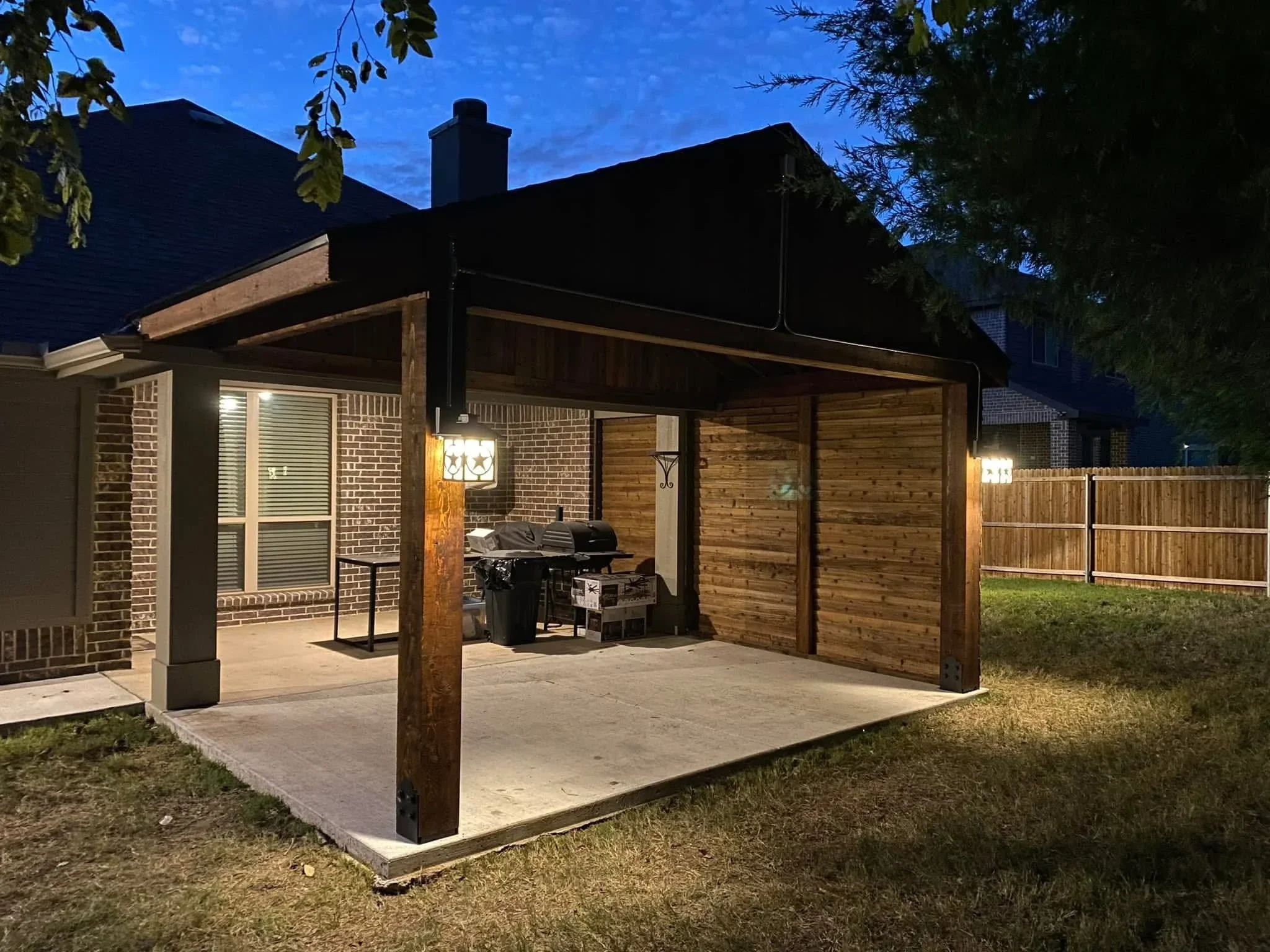 Black steel pergola with retractable shade panels and cedar wood siding over concrete patio