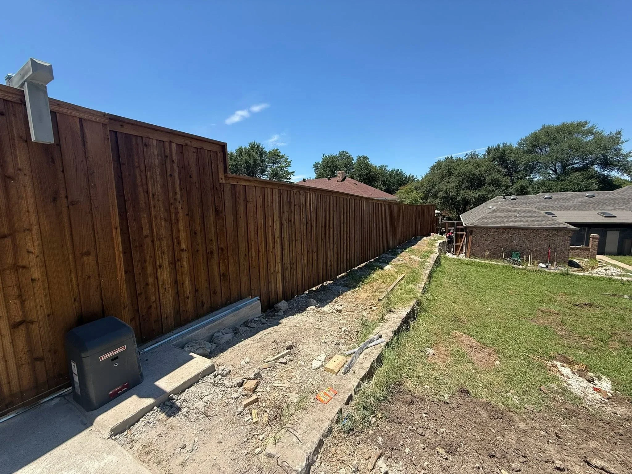 Stained wood privacy fence with vertical boards, concrete footings, and gravel base along residential property