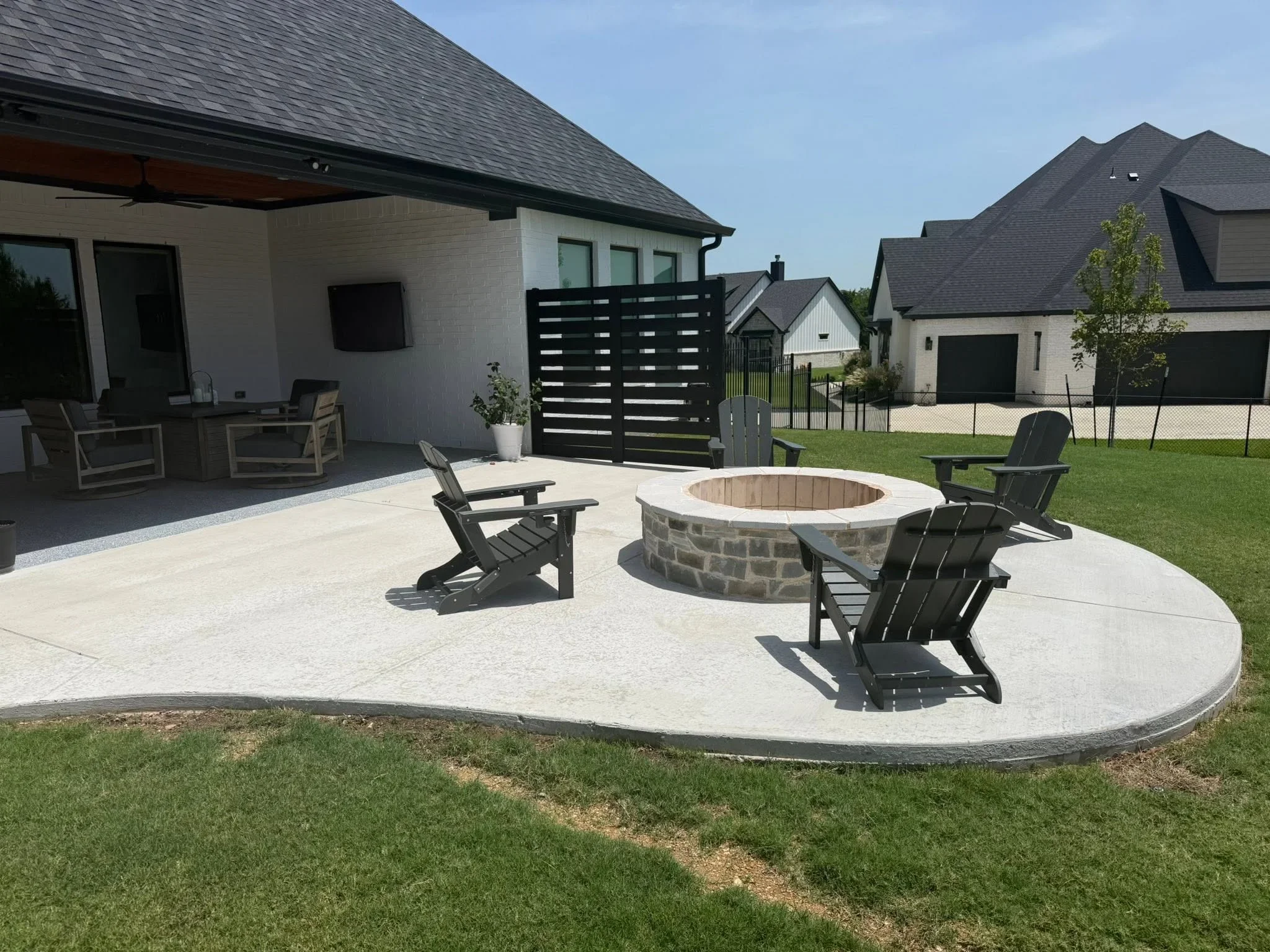 Circular concrete patio with stone fire pit, black privacy fence, and Adirondack seating