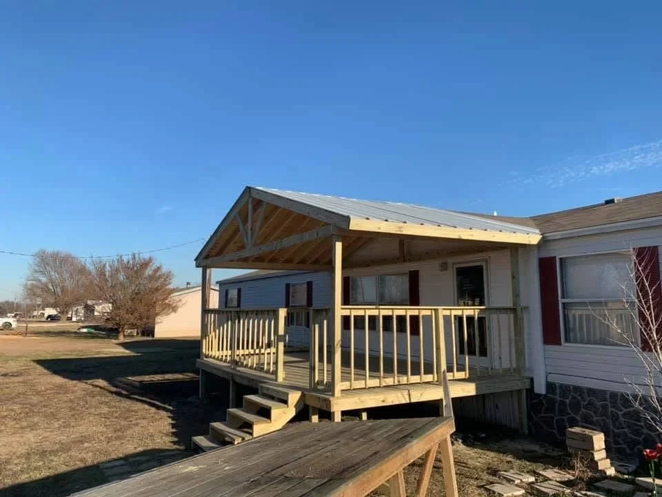 Pressure-treated wood deck with gabled roof porch, railings, and stairs on residential property