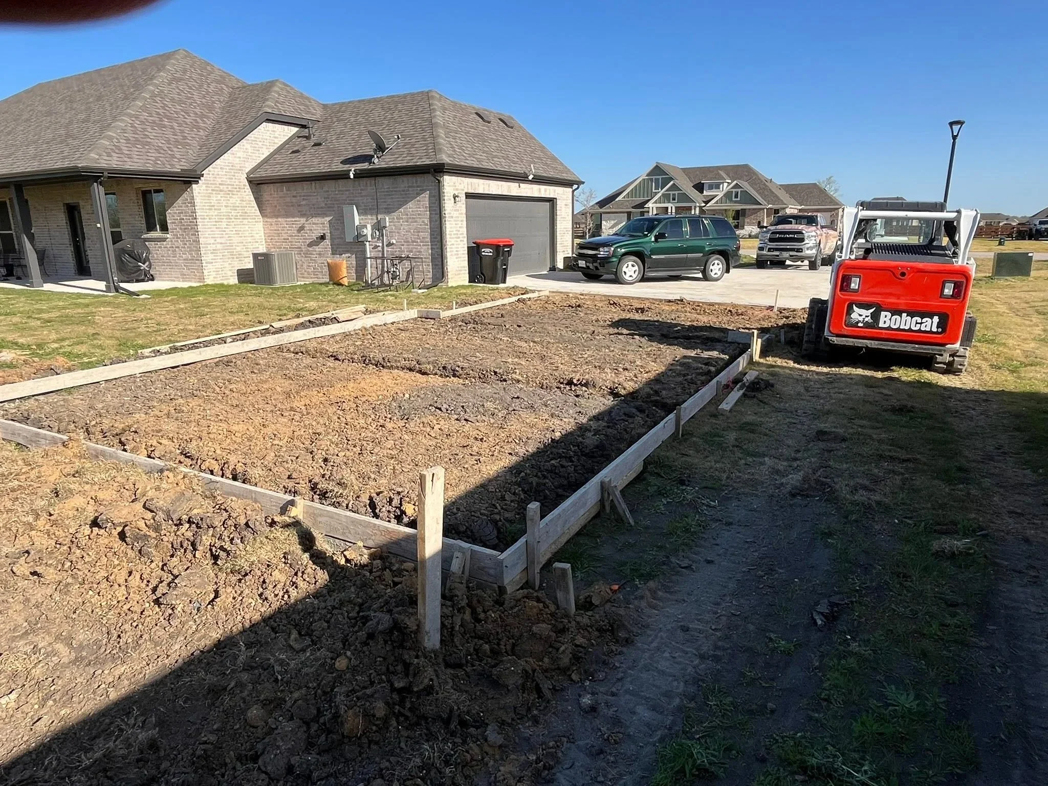 Excavated residential lot with concrete forms, graded soil, and heavy equipment on-site