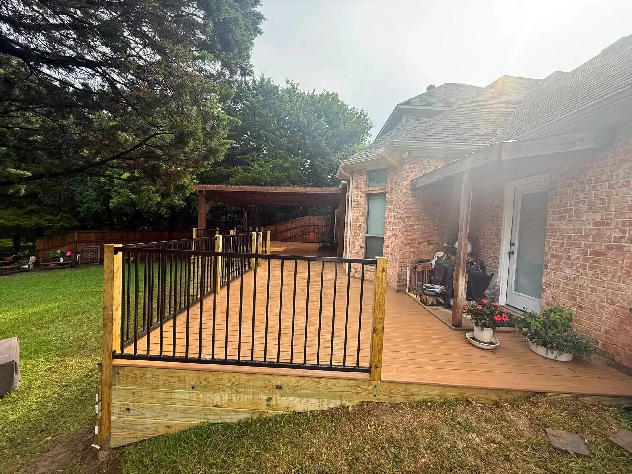 Composite deck with black metal railing, wood posts, and covered structure attached to brick home
