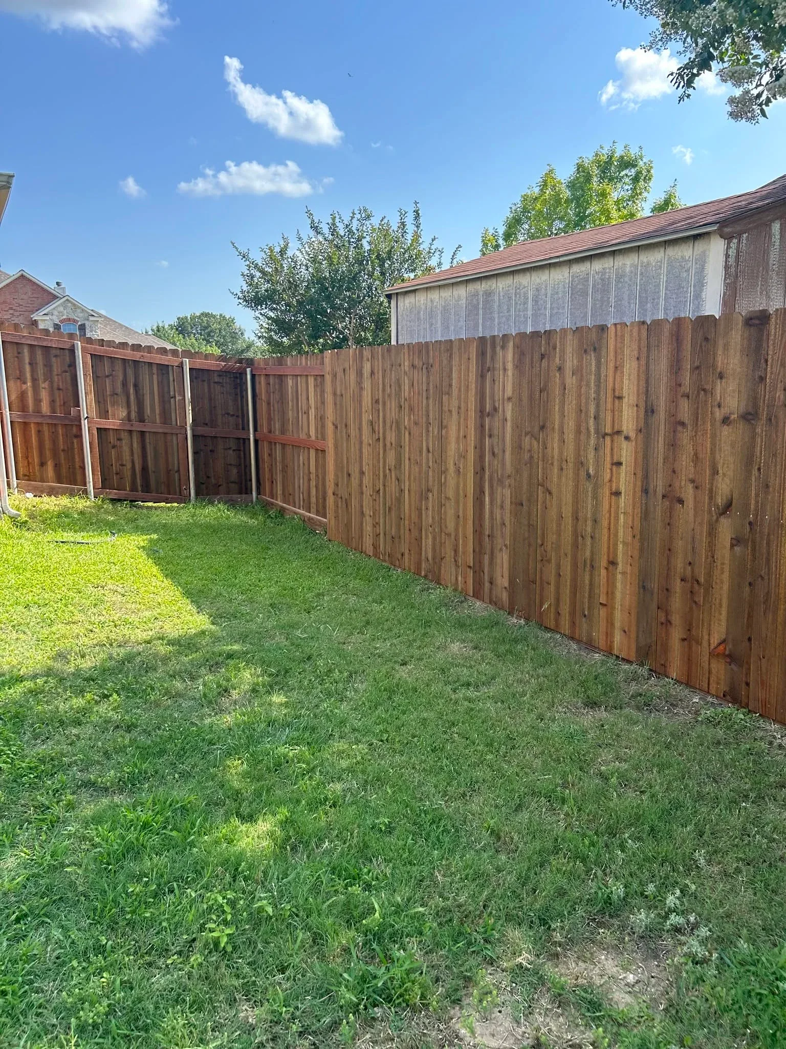 Newly installed wood privacy fence with vertical boards, metal posts, and wooden gate