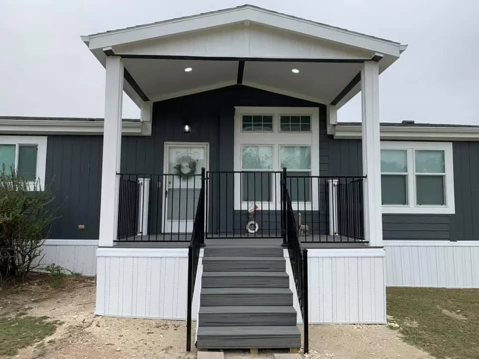 Composite deck with black aluminum railing, gabled roof overhang, and recessed lighting on home entry