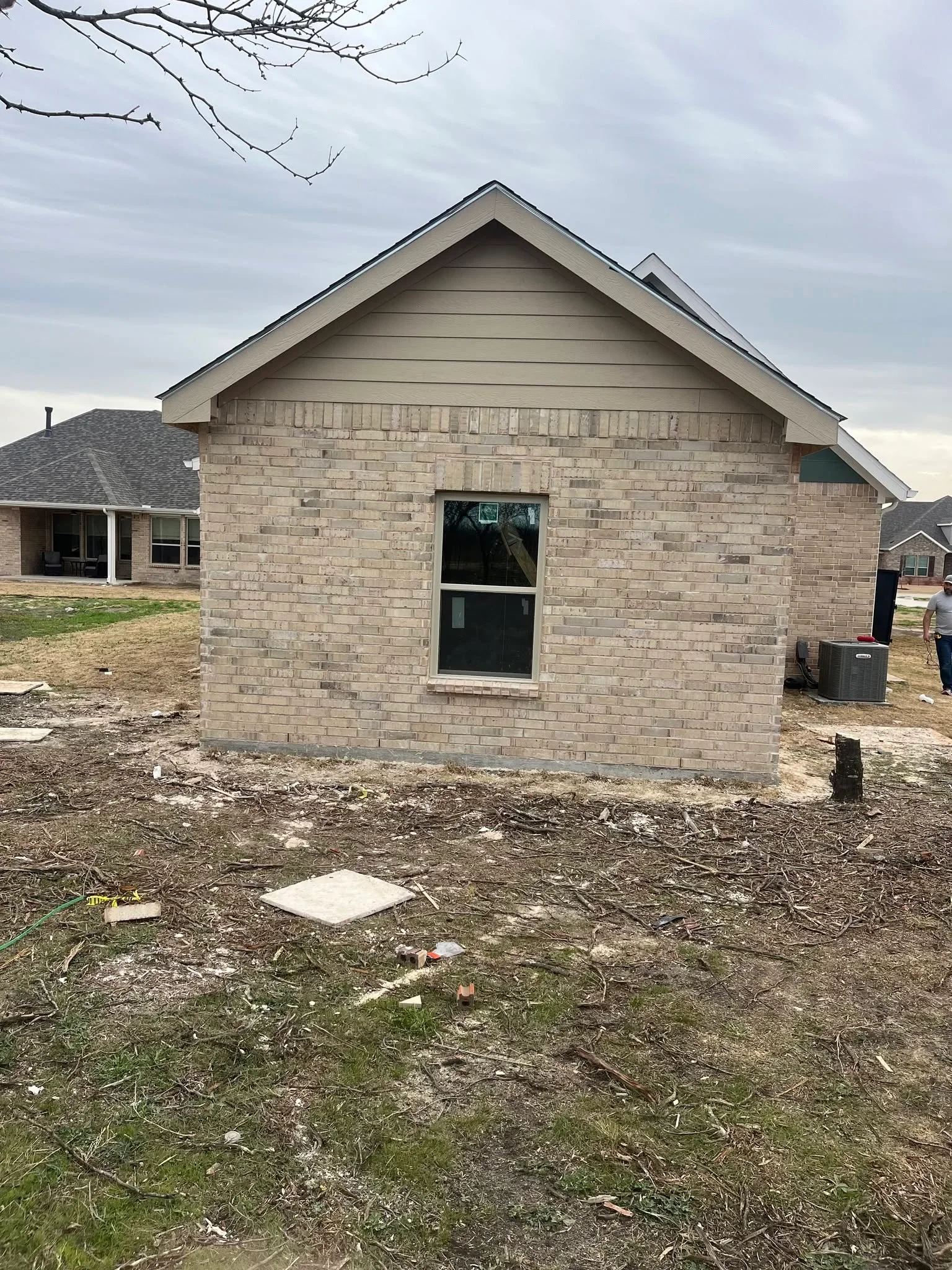 Tan brick addition with gabled roof, window, and door on new construction