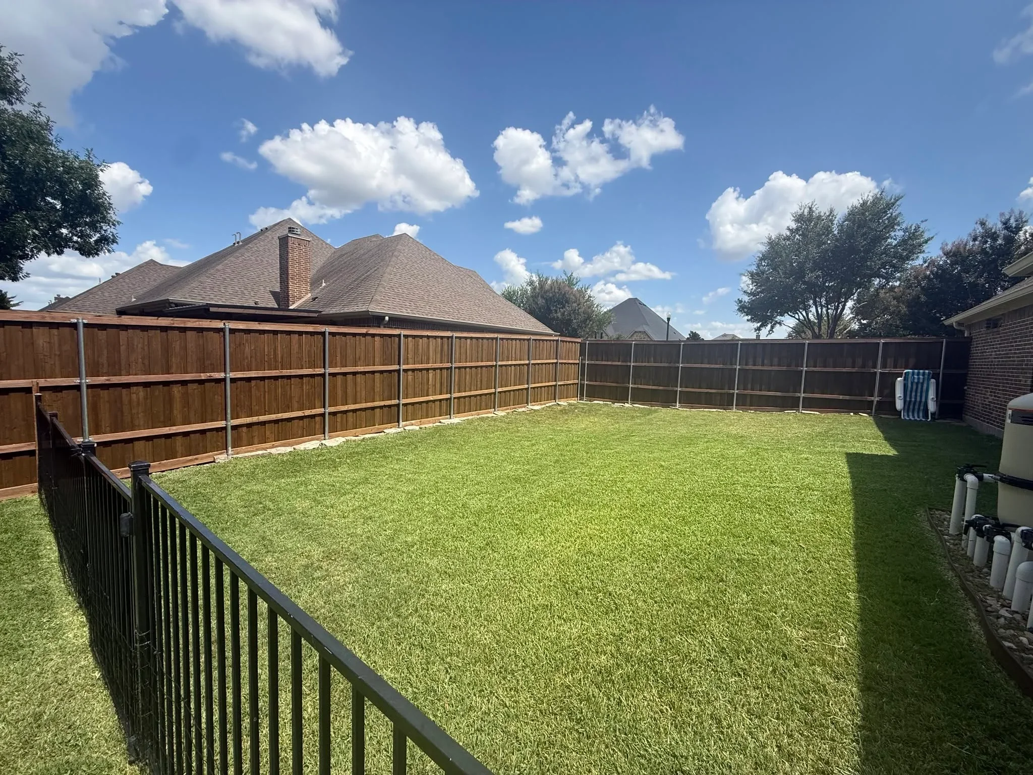 Wood privacy fence panels and black metal railing around residential backyard with green lawn