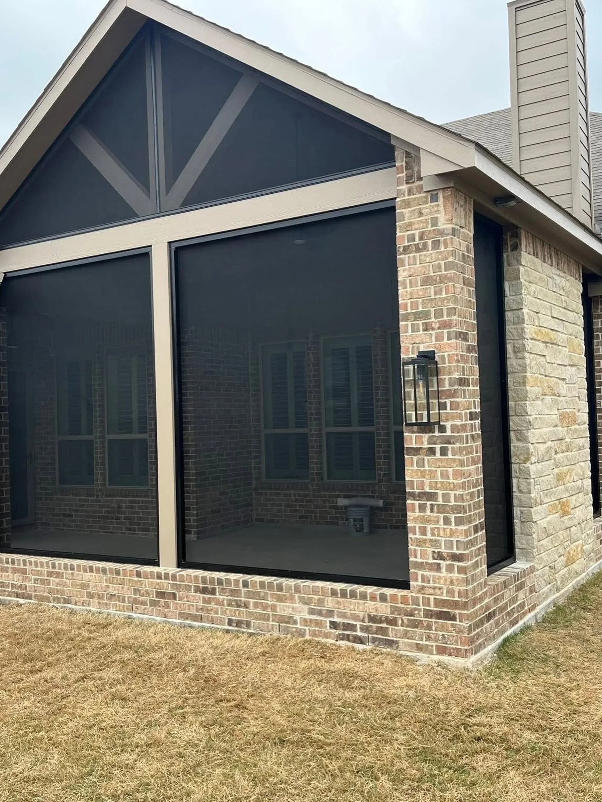 Black aluminum screened patio with mesh panels and brick support columns