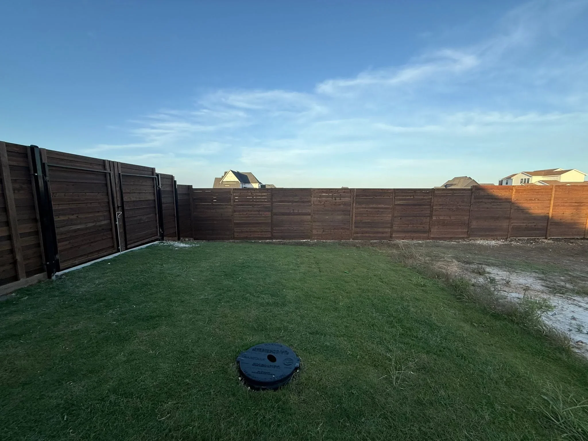Dark brown horizontal wood privacy fence with gate installed around residential backyard with green lawn