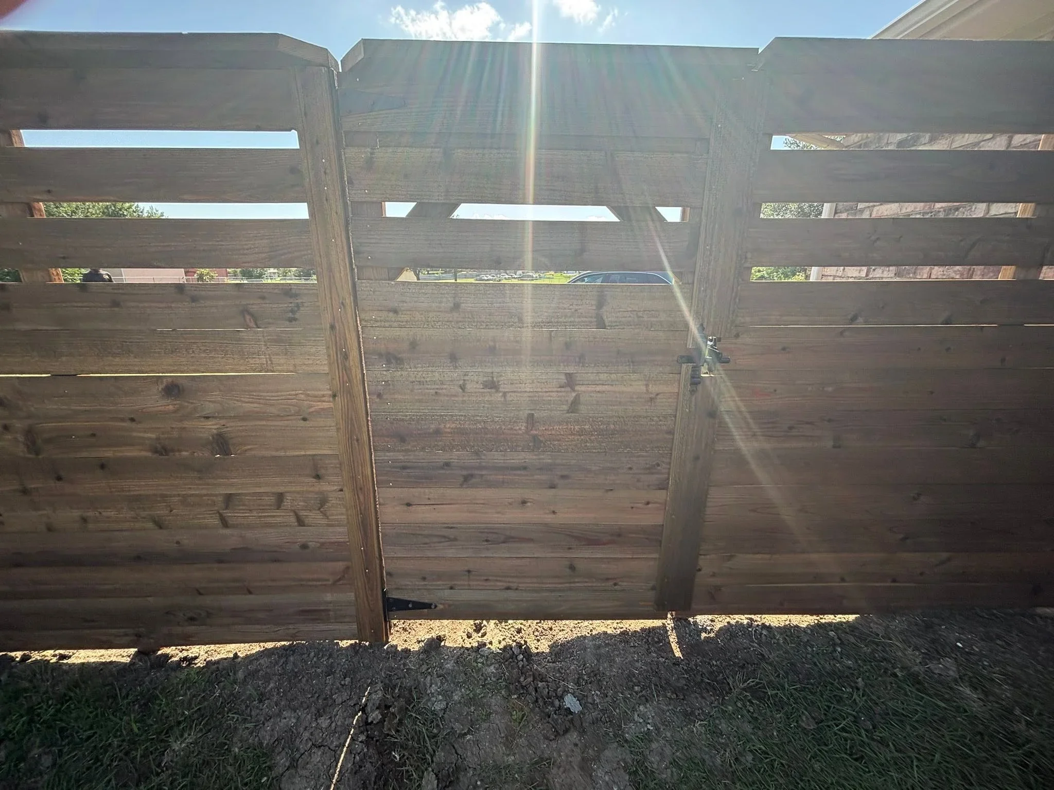 Horizontal wood fence with open slat upper section and solid lower panels, matching gate with metal hardware