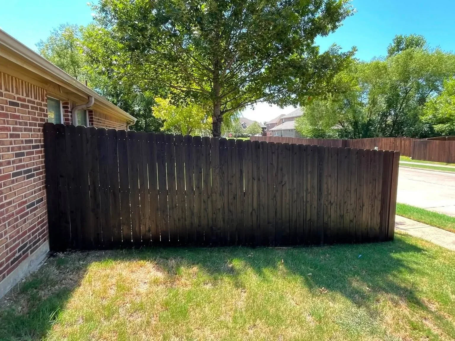Dark-stained vertical wood privacy fence installed along residential backyard property line