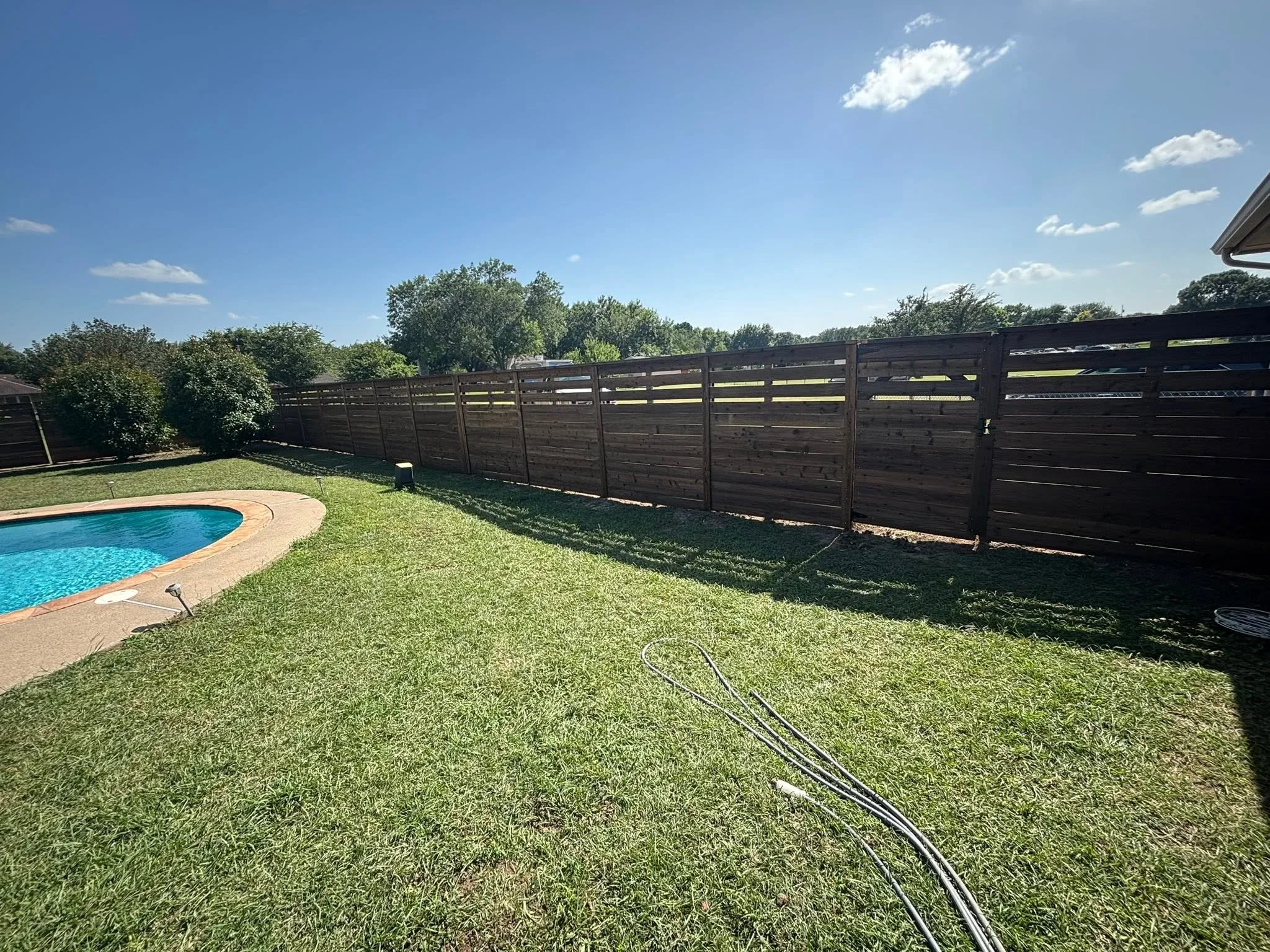 Dark horizontal wood privacy fence with horizontal slats installed along backyard property line