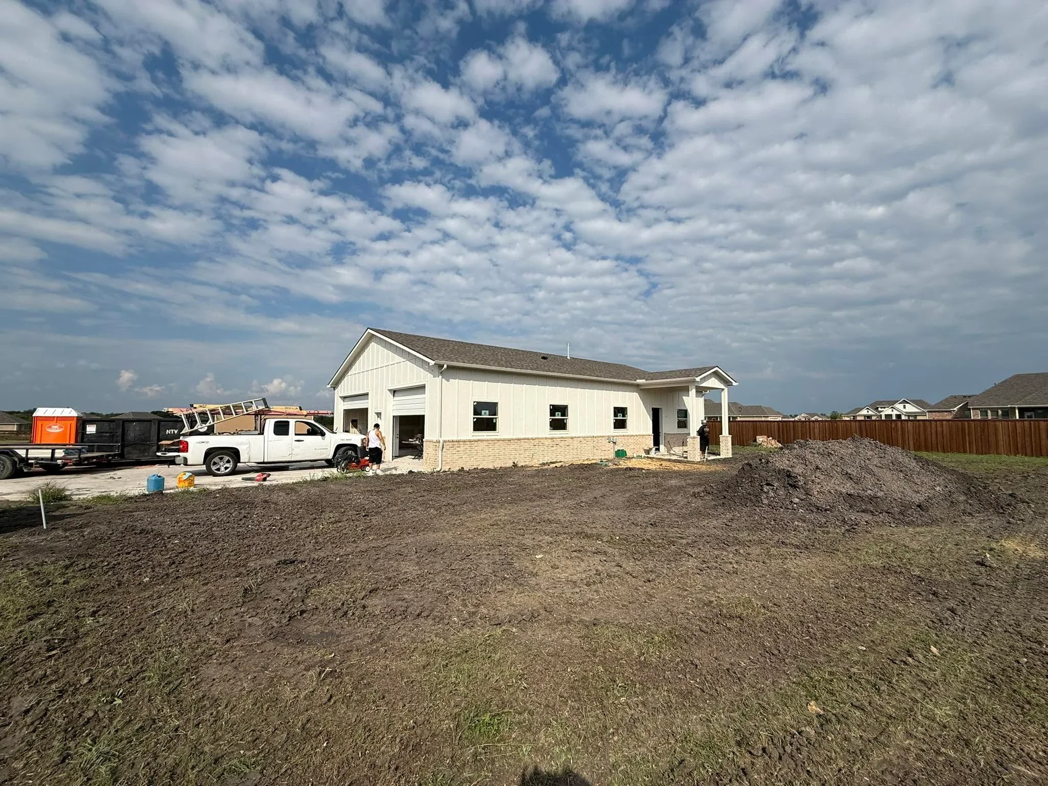 Graded residential lot with new construction home frame, white and tan exterior, dirt foundation preparation