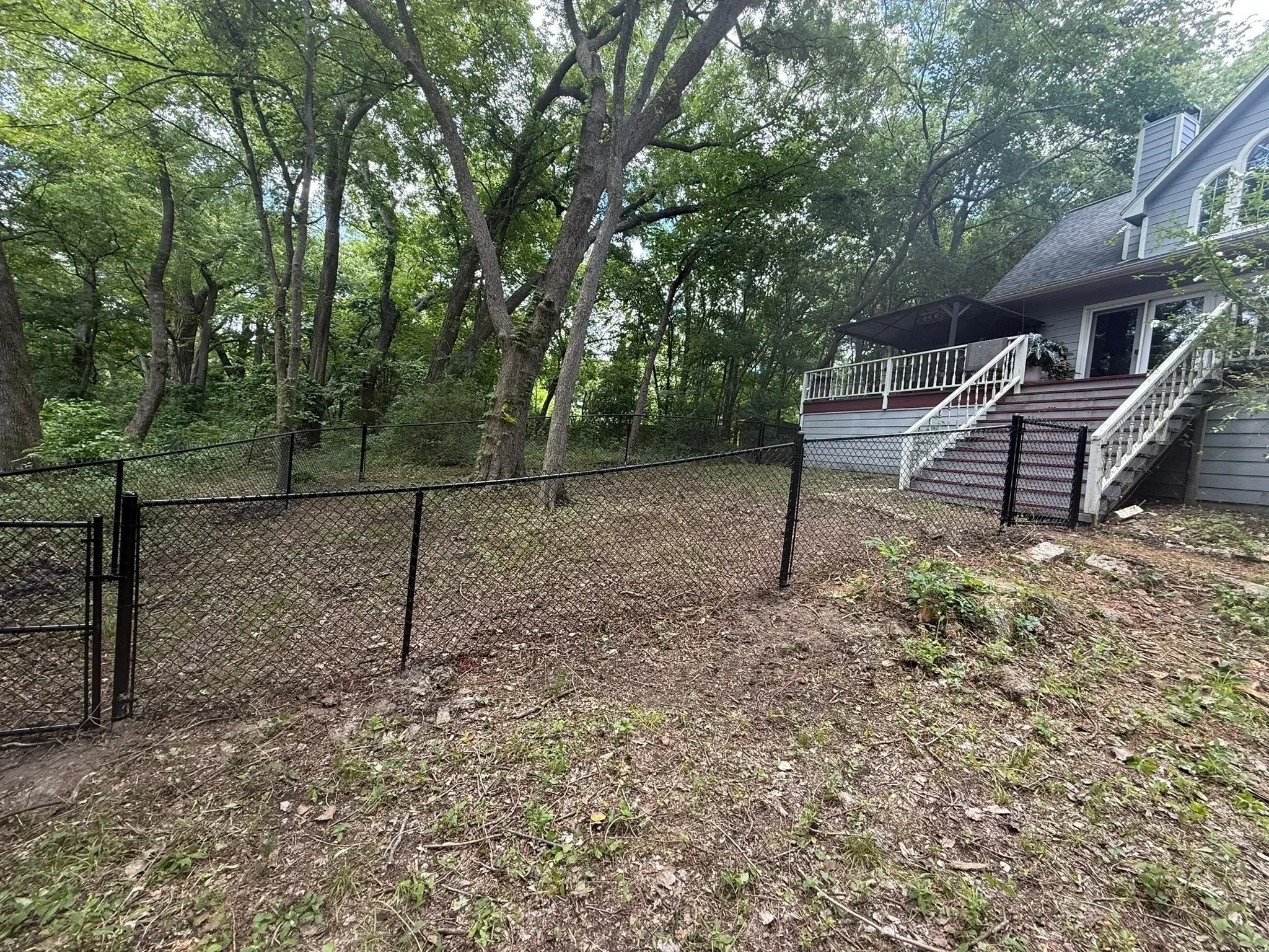 Black chain-link fence with steel posts installed on residential property with mature trees