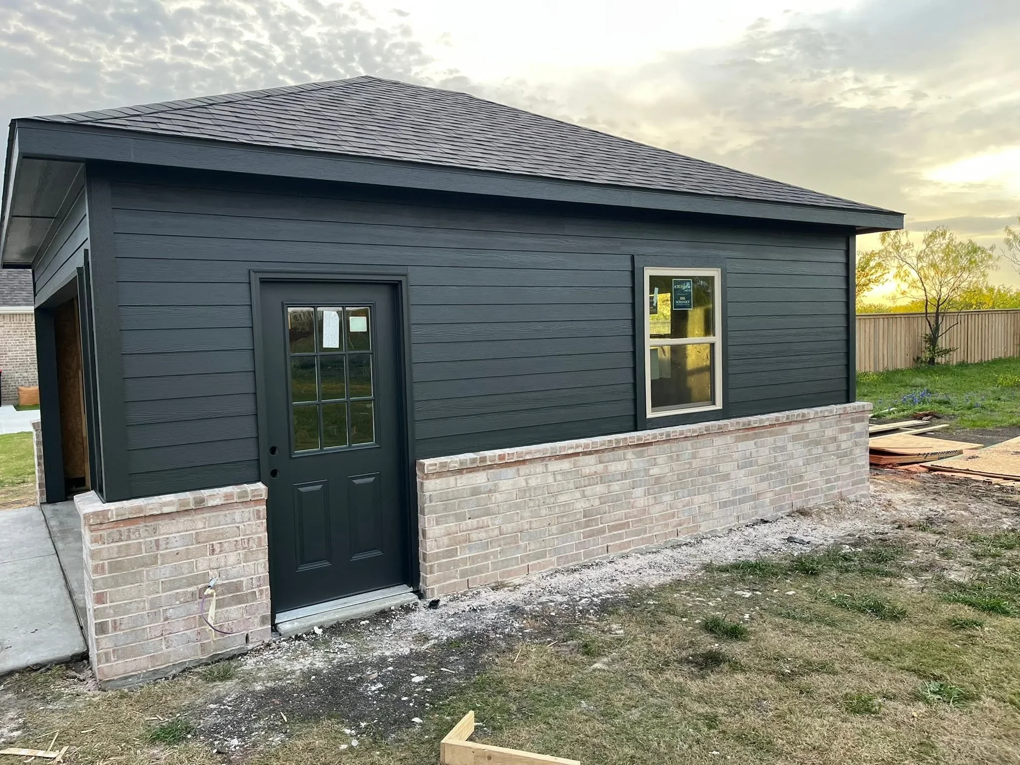 Dark siding garage with brick foundation, architectural shingles, and green entry door