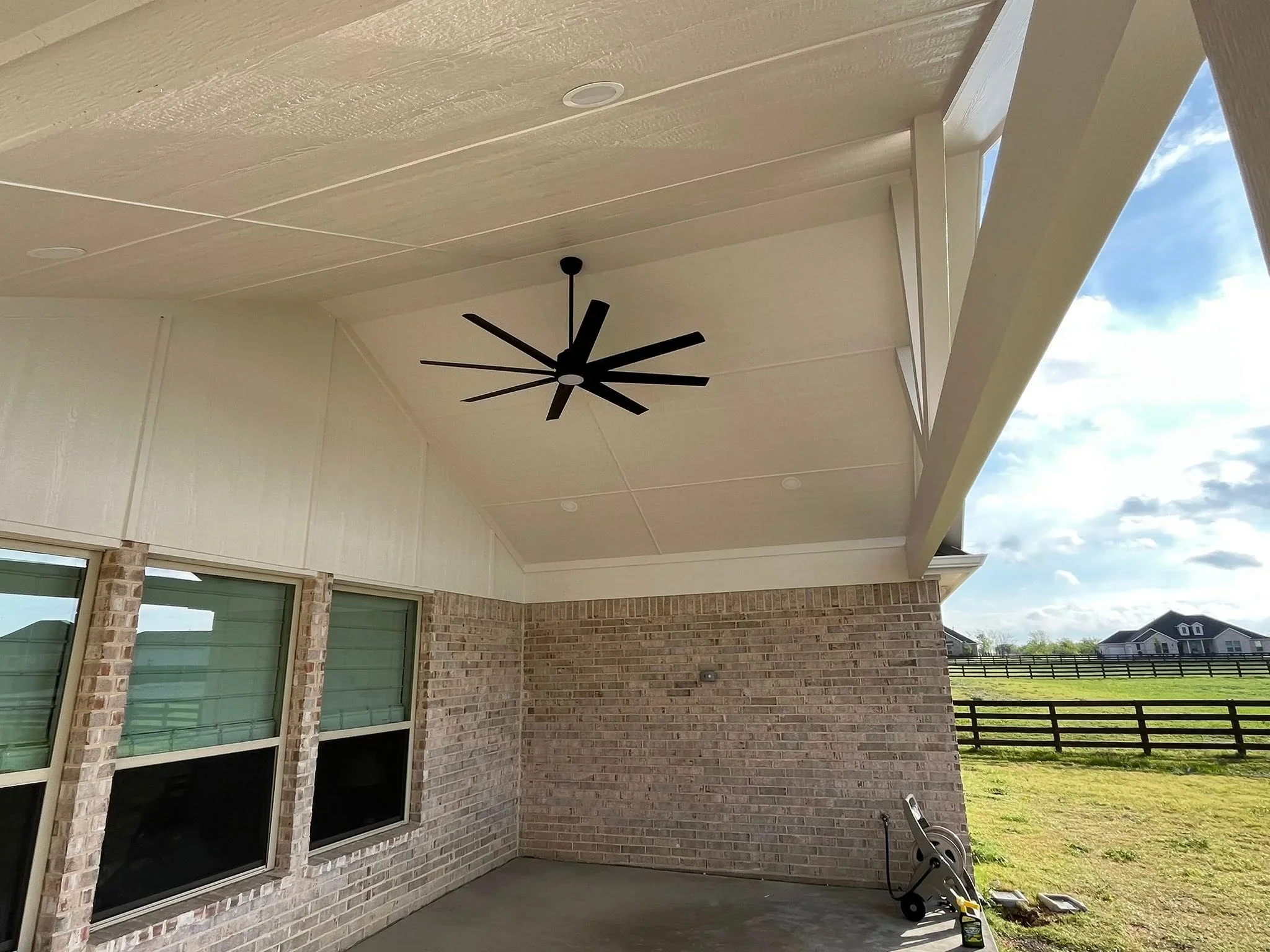 Covered patio with white textured ceiling, black ceiling fan, brick walls, and sliding glass doors
