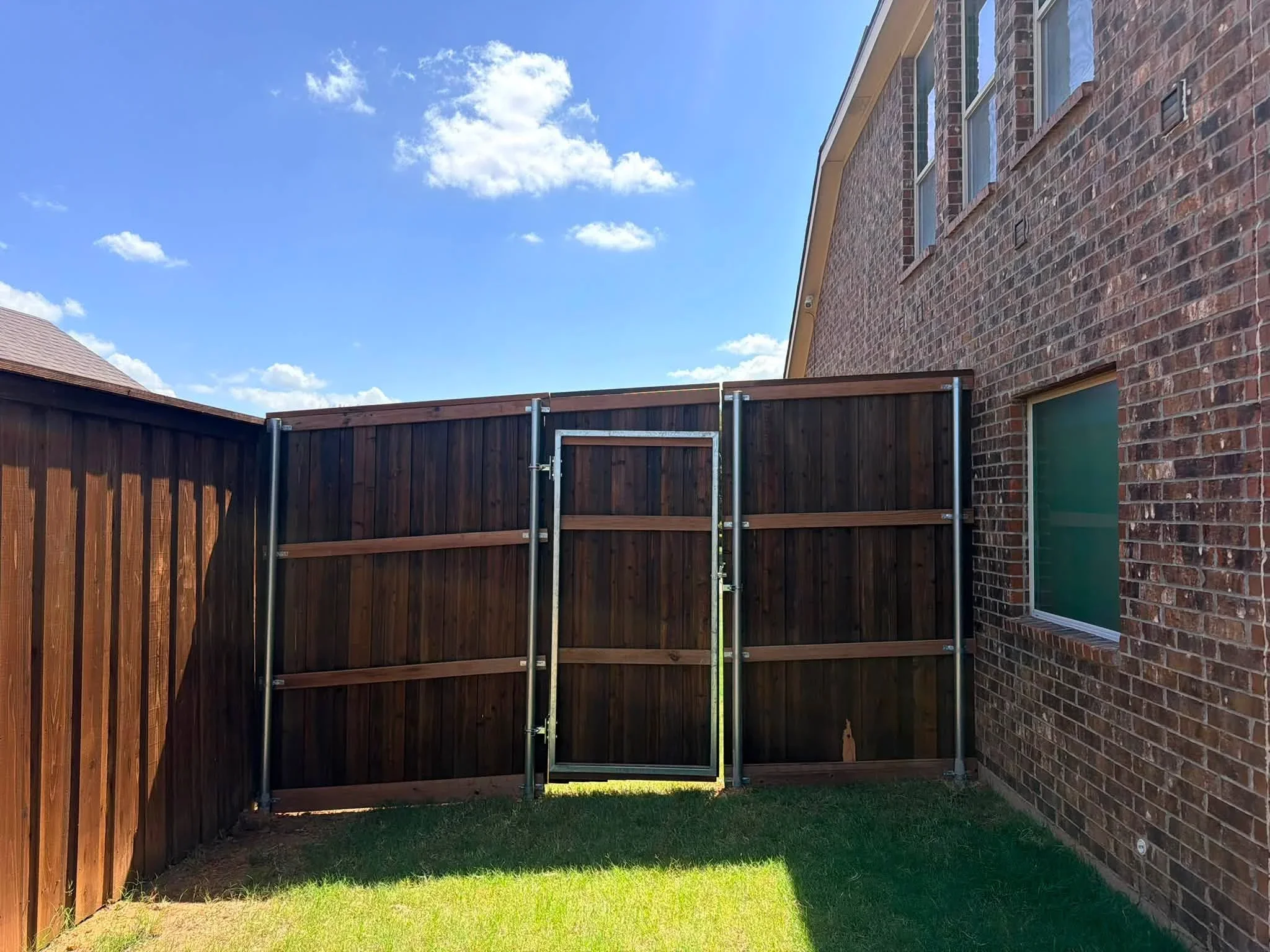 Dark timber fence panels with metal frame gate and horizontal bracing between brick homes
